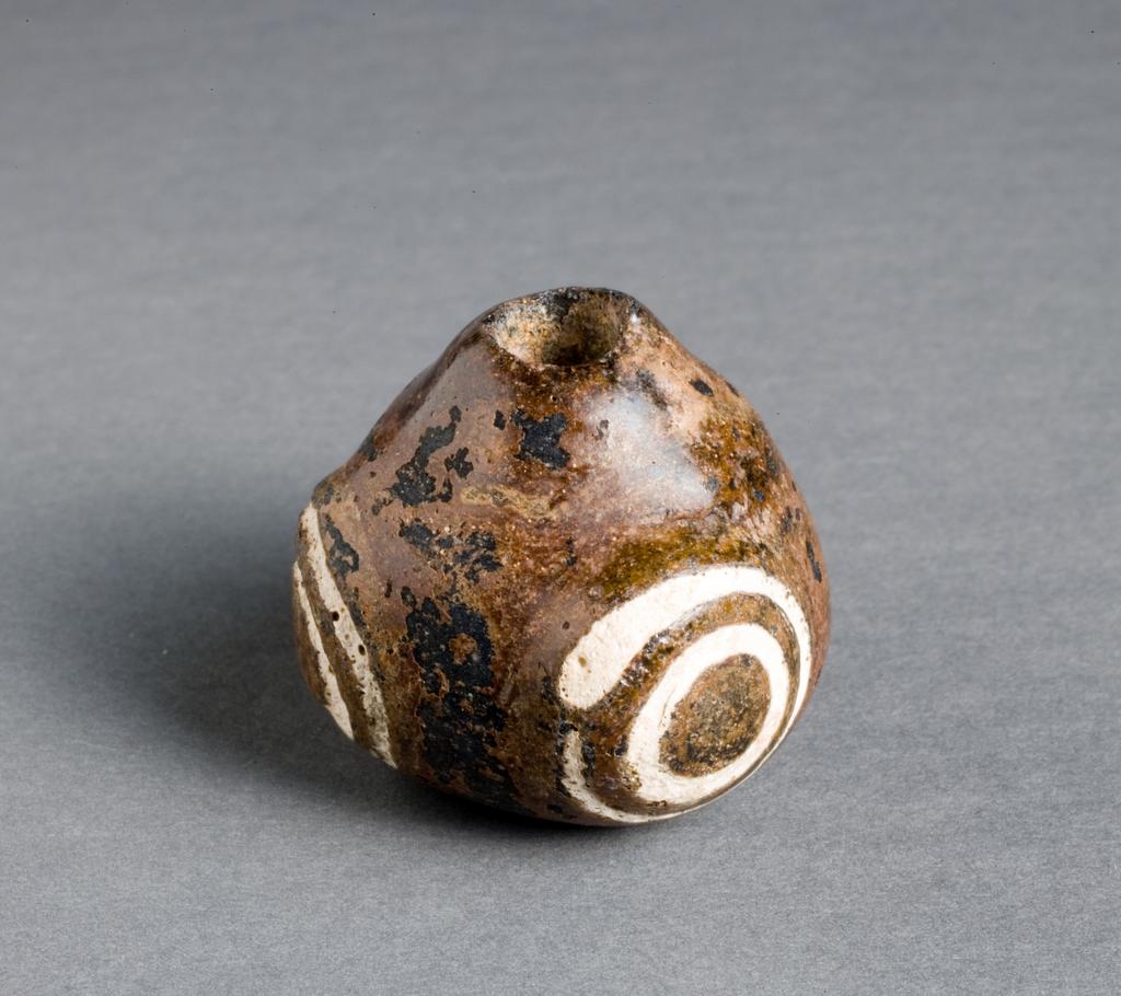 An image of GLASS BEADBead. Three-eyed. Brown glass, pebble-like, with white concentric circles at each of three corners.