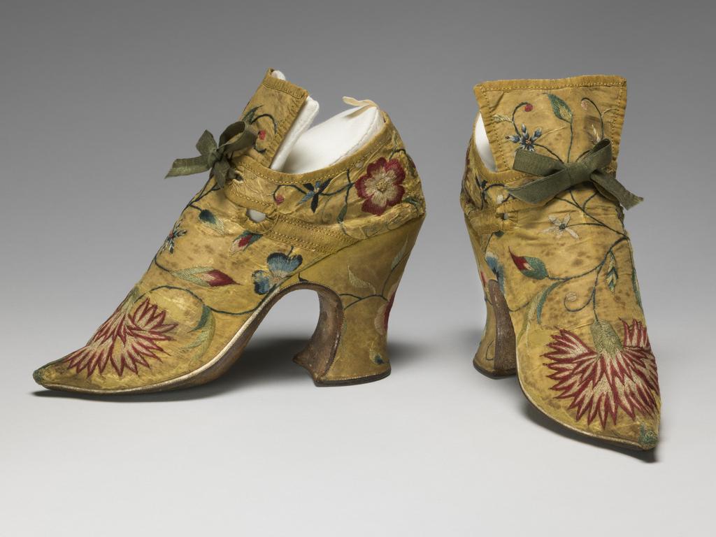An image of Textiles. Shoes/pumps. Silk taffeta, bound with ribbon; floss silk embroidery in French knots, long and short, satin and split stitches; tied with ribbon. Ground covered by a pattern of trailing and scrolling stems with leaves and flowers, carnation, rose, etc., so arranged that there is a carnation on each toe and a rose on each heel with a five petalled blue flower above it. The left shoe has a rose, the right a carnation at each side of the seam. Silk, length, whole, 7 in, height, back, 5.25 in, height, heel, 3 in, circa 1700-circa 1749. English.