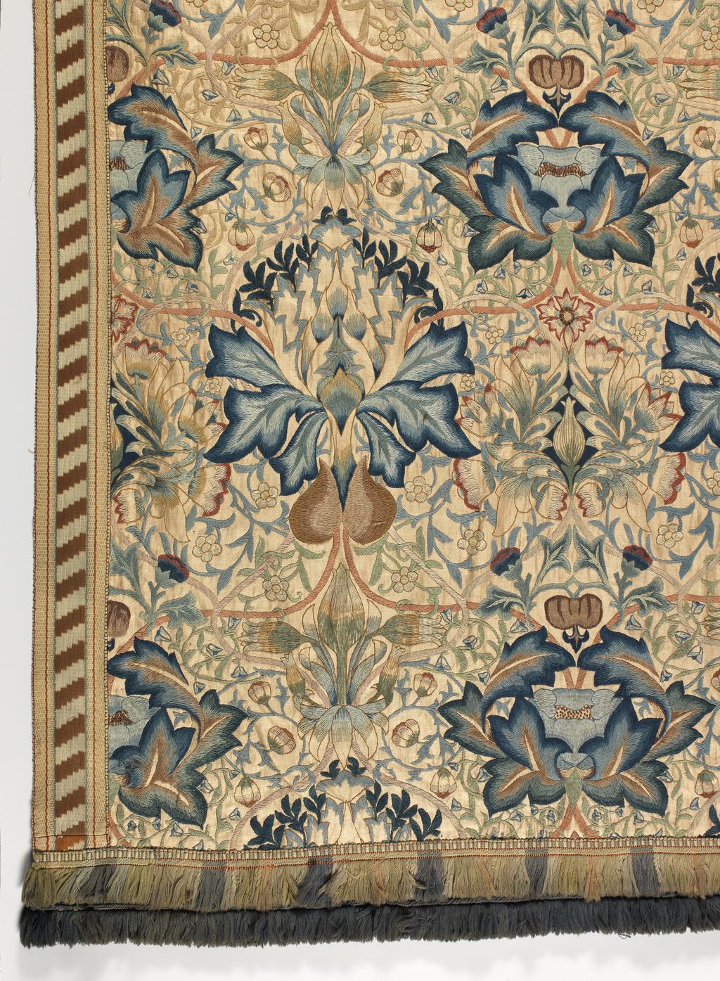An image of Textile. Wall Hanging. Morris, William, designer (British, 1834-1896), Godman, Ada Phoebe, embroiderer (British. Wall hanging, of linen, with polychrome wool embroidery in 'Artichoke' pattern. Linen twill, embroidered in crewel wools in shades of cream, beige, pale, medium and dark brown, yellowish-brown, pale yellow, salmon pink, pale, medium and dark rose pink, pale, medium and dark green, pale medium and dark Prussian blue, pale blue, grey, and white with Artichoke design incorporating stylized artichokes, other flowers, and foliage. The borders are of oblique stripes, and the lower edge is fringed. Height (whole) 213.5 cm, width (whole) 983.6 cm, circa 1875-circa 1899. Arts and Crafts. Notes: The design of 1877 entitled 'Mrs Godman. Design for embroidered hanging (artichoke design)' is in the Victoria & Albert Museum (65-1898). This hanging and the other pieces which covered the walls of the room were worked by Mrs Godman over about twenty-five years.