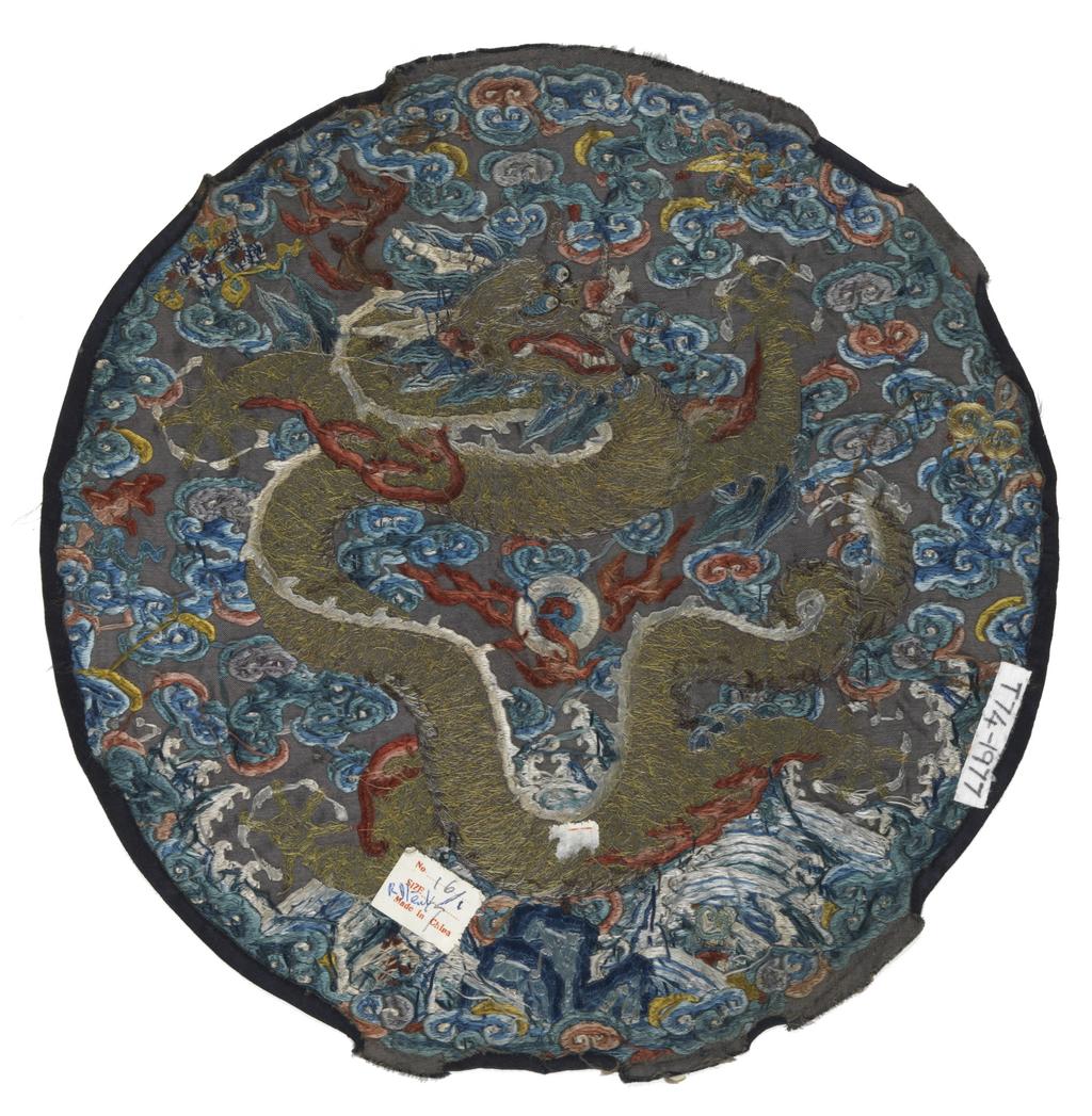 An image of Textiles. Roundel. Unknown maker, China. Five-clawed dragon on a background of waves and clouds, with six precious objects around perimeter. Silk and metal embroidery on satin; blue ground with polychrome embroidery - satin stitch, stem stitch, encroaching satin, seed stitch (Peking knot), with laid and couched work. Diameter, whole, 28 cm, circa 1750-circa 1775. Acquisition Credit: Given by Mrs. Soame Jenyns, in accordance with the wishes of her late husband, Soame Jenyns.