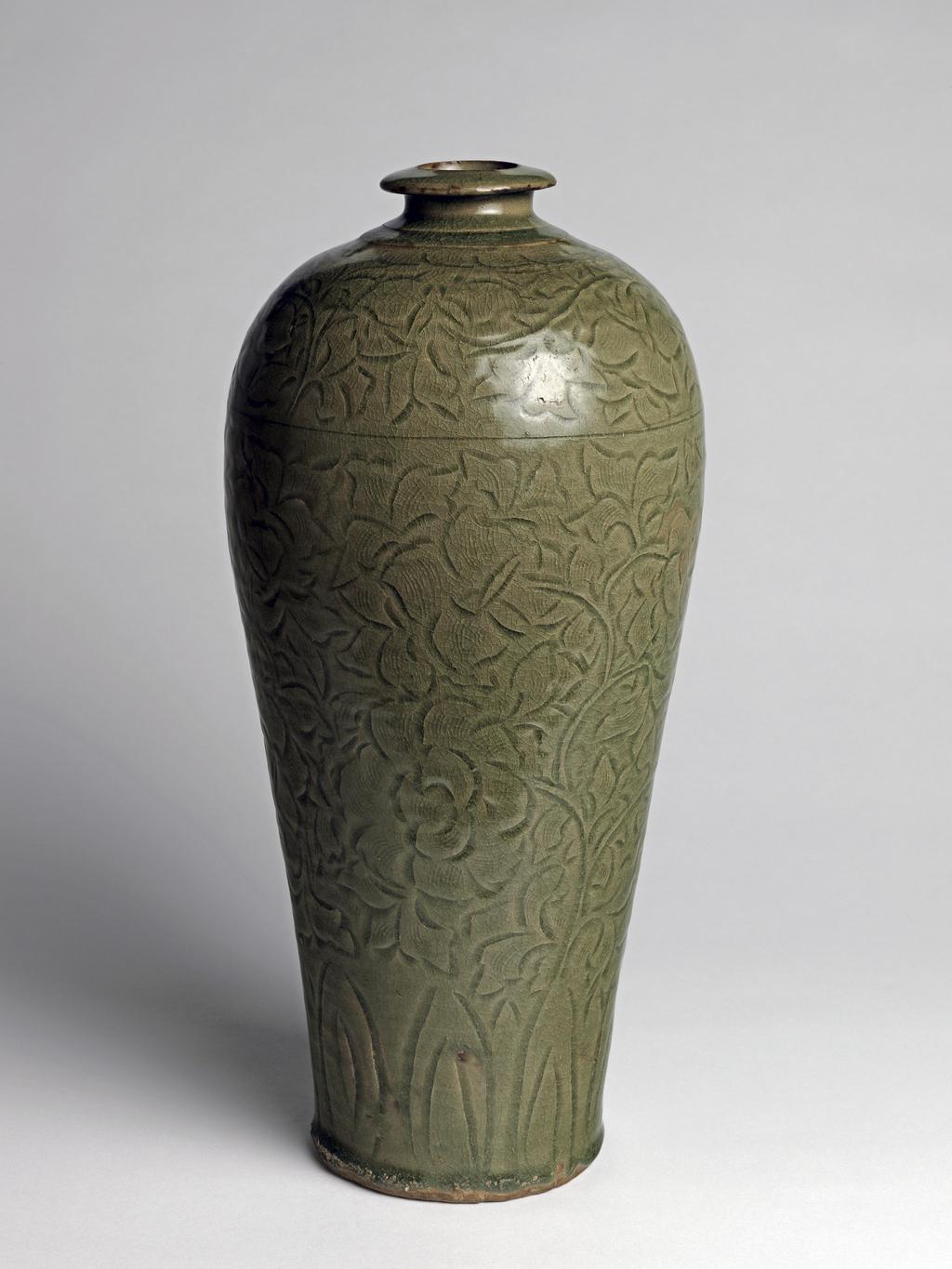 An image of Tall stoneware vase. Northern Celadon type with a brownish green, finely crackled glaze. The body is grey with incised and combed decoration of stiff leaves round base below peonies and foliage.  There is a leaf scroll band round the shoulder, as well as a brown mark. The lip is everted and downward sloping. The base is recessed and glazed, with kiln sand attached. The rim is unglazed. Stoneware, celadon glazed, incised, height 42.5 cm, diameter 19 cm. Song Dynasty (960-1279). Chinese.