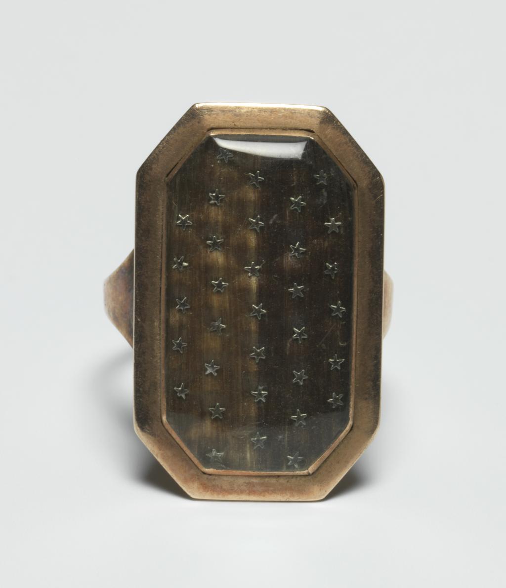 An image of Jewellery. Ring/Mourning Ring. Gilt-metal, plain, narrow hoop, broadening at shoulders. Long octagonal bezel, containing under glass, hair of two different colours set with rows of small metal stars. Inscribed on the back: 'NB Toms Ob 19 Dec 1794 At 5ys W: Toms ob: 28 Mars 1786 Aet 11 ys'. Height, hoop, 1.5 mm, depth, hoop, 1.0 mm, length, hoop, 21.0, mm, height. bezel, 27.0 mm, length, bezel, 17.0 mm, width, bezel, 4.5 mm, 1786. English.