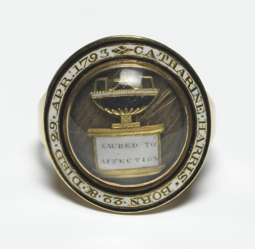 An image of Jewellery/Mourning ring. Gold hoop, expanding at shoulders. Circular bezel. Round the edge, reserved in white enamel, bordered at both edges with a narrow band of black enamel, is in the inscription: CATHERINE. HARRIS. BORN 22. 8C. DIED. 29. AP: 1793. At the centre, under glass, on a background of hair, an urn on a pedestal, inscribed 'SACRED TO AFFECTION'. Urn composed of gilt-metal, black and white enamel. Gold, hair, enamel and gilt-metal, height, hoop, 2.0, mm, depth, hoop, 1.25, mm, length, hoop, 21.0, mm; height, bezel (circular) 5.0 mm, length, bezel (circular) 20.0, mm, width, bezel (circular) 20.0 mm, 1793. English.