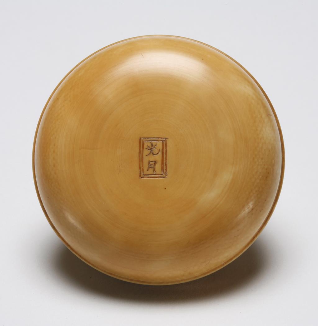 An image of Manju. Unknown maker, Japan. There are two halves of this Manju, one is the scene of farmers working with the water mill pumping river water for irrigation of the farm, the other half is the scene of two villagers in a house enjoying tea underneath bamboos and pine trees. These two halves can be screwed tight together. Ivory, carved, 1800-1899.