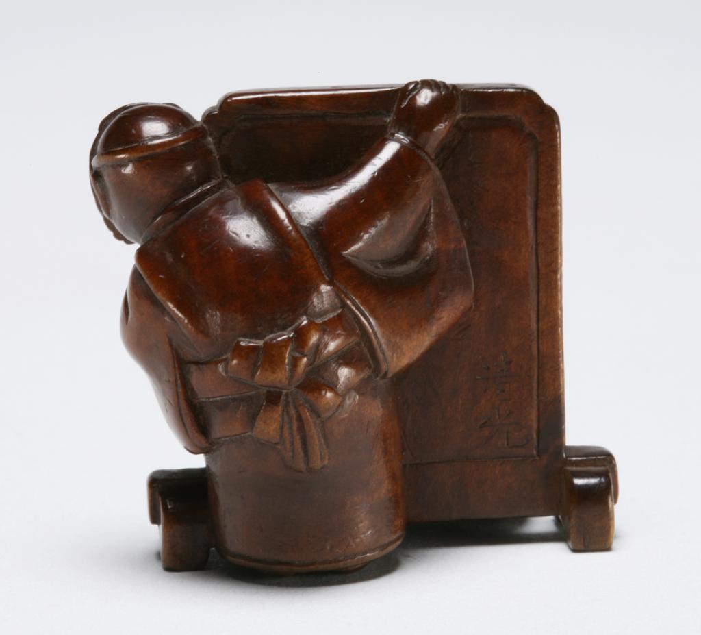 An image of Netsuke: katabori: Figures and screen. Kiyomitsu (Japanese). Group of two figures playing kakurembo (hide-and-seek), one curled in a ball, face down, his hands over his head hiding behind a screen; the other standing barefoot in a kimono, his face covered by a grotesque mask and peering round the side of the screen which is carved with a large peony head, bud and leaves. Standing figure's outspread arm resting on the screen forms a natural himotoshi. Good patina. Wood, carved, height, whole, 3.6 cm, width, whole, 3.4 cm, circa 1868-1900. Edo Period (1615-1868).