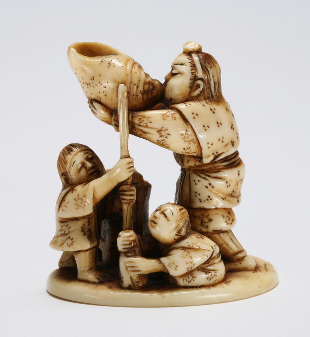 An image of Netsuke. Unknown maker, Japan. Yamabushi (the wandering fighting priest) blowing a giant conch shell, while two young boys possibly attendants waiting and playing next to him. Ivory, carved, 1830-1870.