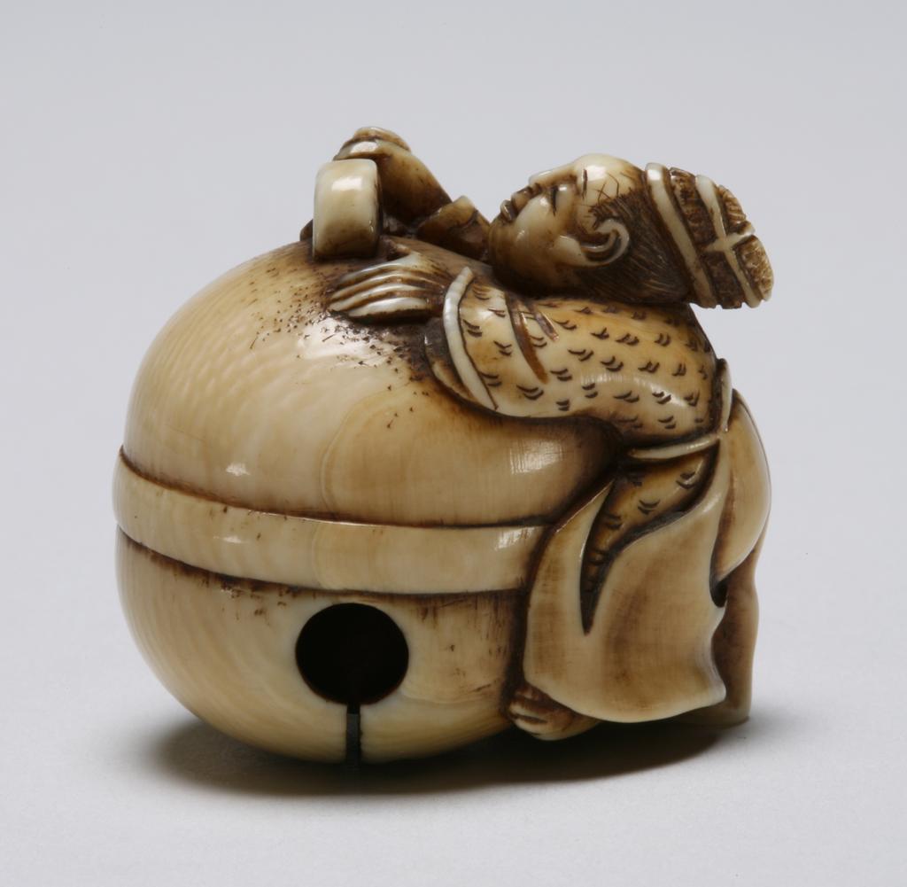 An image of Netsuke. A large round temple bell being polished by the attendant. A loose ball inside the bell. Unknown maker, Japan. Ivory, carved, 1800-1900.