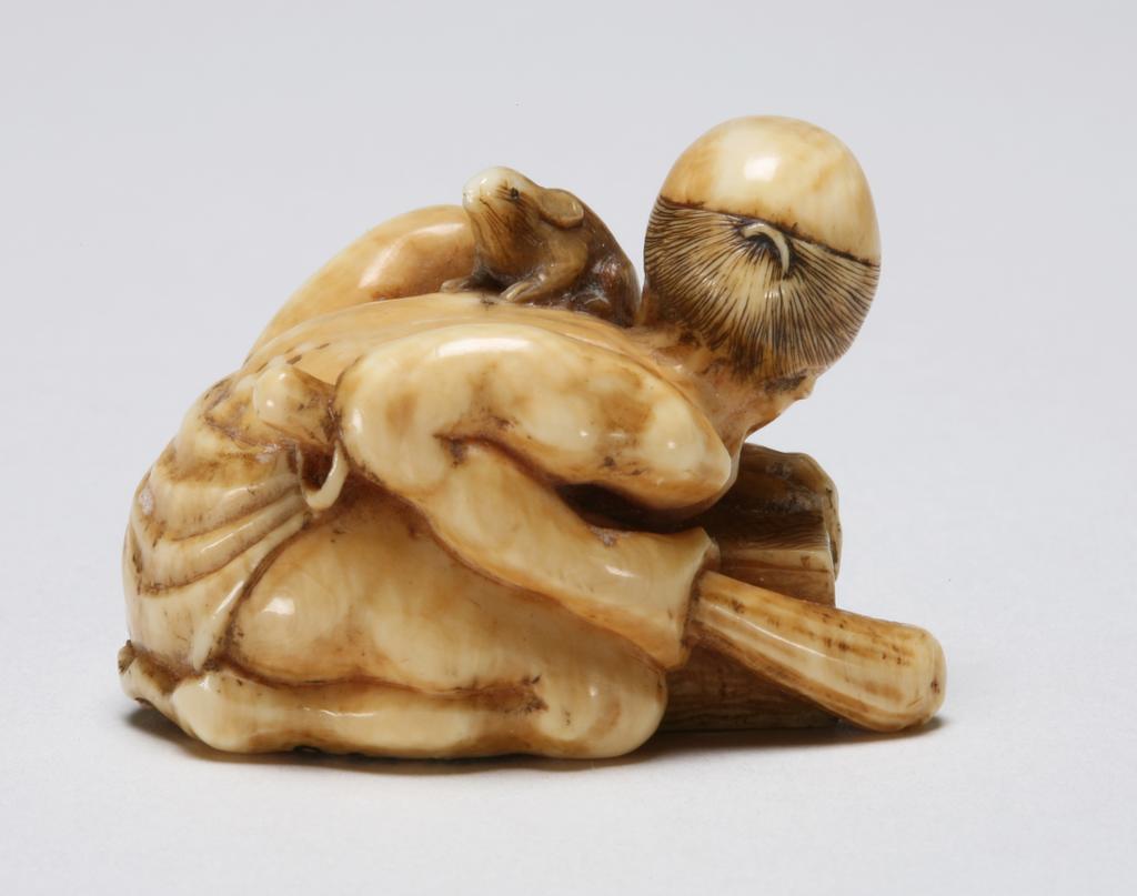 An image of Netsuke: katabori: Rat catcher. Masakazu, Edo Period, 19th century, Japan. Figure of an angry rat catcher half-nude crouching over a grain-measure holding a large club in his right hand and looking at the rat escaping over his left shoulder. The rat with finely incised details and black eyes, the man with a shaven head and his hair scraped into a bun; his tongue and eyes are tinted red. Himotoshi through the back of the grain-measure. Ivory, finely carved, incised and stained, height, whole, 2.6 cm, width, whole, 3.7 cm, circa 1800-1868. Edo Period (1615-1868).