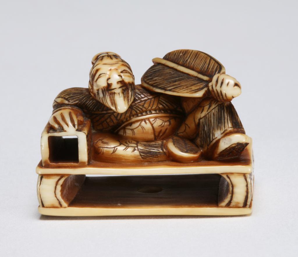 An image of Netsuke. Rosei asleep dreaming on his magic pillow, holding a fan in his left hand. Unknown maker, Japan. Ivory, carved, 1800-1900.