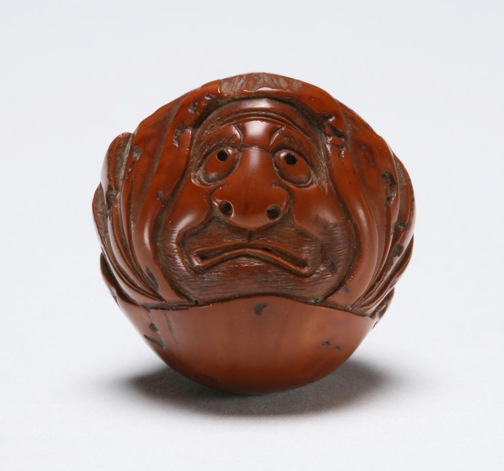 An image of Netsuke. Katabori. Seated Daruma. Issan (Japanese). Figure of Daruma, seated and enveloped in his voluminous cloak bearing a sad, resigned expression. Pierced nostrils and inlaid horn eyes. Himotoshi at the centre back. Wood, spherical and hollow, inlaid decoration, height, whole, 2.7 cm, width, whole, 3.0 cm, 1800-1830. Edo Period (1615-1868).