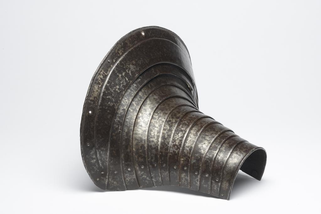 An image of M.9-1945: Armour. Defence for the left foreleg of a horse, for heavy cavalry use. Unknown production, Germany. Formed of twelve downward-overlapping lames curved to the front of the horse's upper foreleg and shoulder, and increasing in width to its upper end. The upper edge of the top lame is slightly convex with gently rounded corners. It has a file-roped inward turn accompanied by a recessed border containing nine holes for lining-rivets, of which six are occupied by externally-flush rivets. The lower edge of the bottom lame also has a file-roped inward turn. The outer ends of the lame on each are fitted with externally-flush rivets that formerly served to secure a strap around the rear of the horse's leg. The first to eleventh lames have bevelled outer edges. The lames are connected to one another at their outer ends by externally-flush sliding-rivets. The lames were further connected to one another by a pair of internal leathers located a short distance within the sliding-rivets. The leathers were attached to each lame by single externally-flush rivets. The rivets for the outer leather are preserved in the ninth to twelfth lames, and for the inner leather, in the eighth and ninth lames. The leg-defence has a ' black from the hammer' finish, now much worn, particularly at the centre of its lower half. Steel, hammered, shaped, riveted, with file-roped, recessed border and bevelled decoration. Height, whole, 25.5 cm, maximum, width, whole, 29.1 cm, maximum, depth, whole, 22.1 cm, maximum, weight, whole, 1.02 kg, circa 1550. Provenance: From the armoury of the Princes Radziwill, Castle of Niescwiez, Poland. Notes: forming a pair or near pair to M.14-1947. 

M.14-1947: Armour. Leg-defence for the right foreleg of a horse. Unknown production, Germany. Formed of twelve downward-overlapping lames curved to the front of the horse's upper foreleg and shoulder, and increasing in width to its upper end. The upper edge of the top lame is slightly convex with gently rounded c