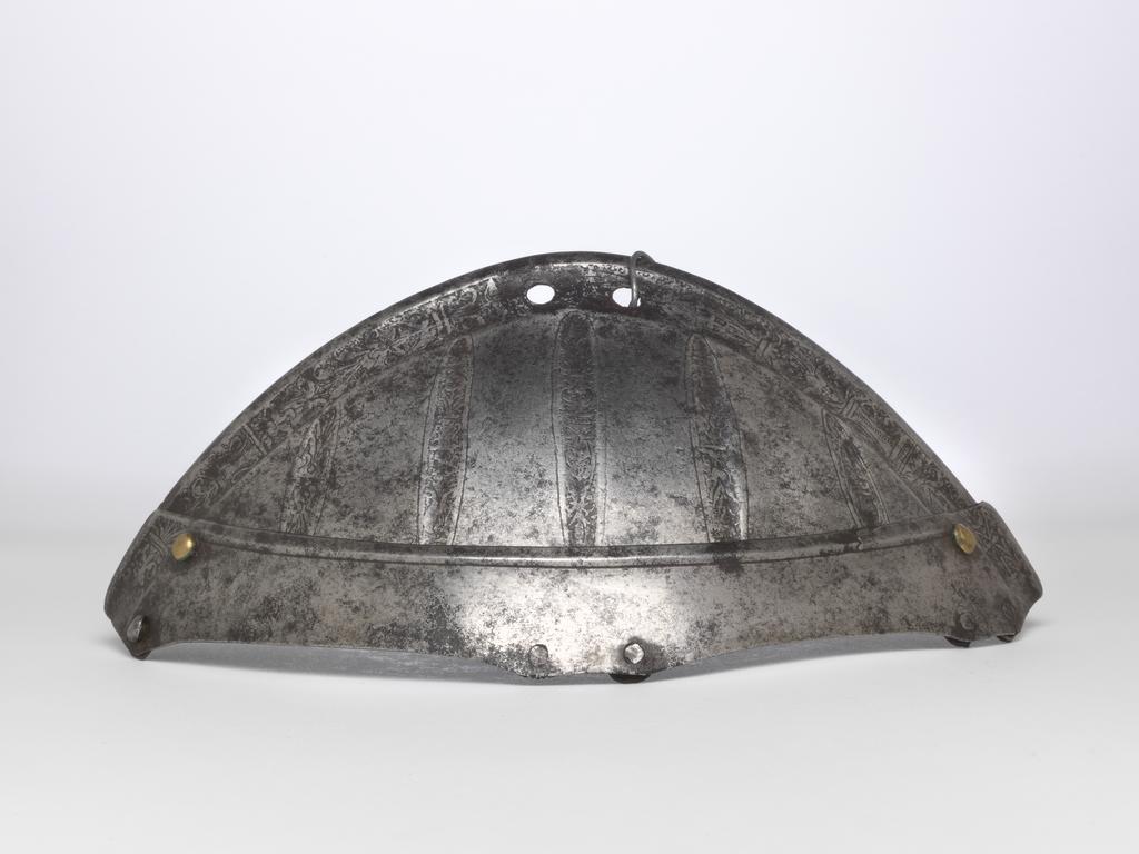 An image of Armour. Top two lames of a spaudler for the right shoulder, for parade use, with 'puffed-and-slashed' decoration in imitation of civilian costume. Production Place: South Germany. Helmschmied, Koloman, armourer, possibly (German, 1470/71-1532). Consisting of two upward-overlapping lames of which the first is considerably deeper than the second and has a convex upper edge running into the lateral edges of the latter. This edge has a plain, partial inward turn accompanied by a recessed border decorated with an etched 'candelabrum' design on a plain, blackened ground. The first lame is decorated below this border with five, slender, vertical 'slashes' in imitation of those found on contemporary civilian costume. The upper edge of the second lame has a plain, partial, inward turn between the main borders at its outer ends. The lames were formerly connected to one another and to successive lames by brass-capped, round-headed rivets with irregular, internal washers at the rear, and by internal leathers secured to each lame by pairs of externally-flush rivets at the front and centre. All the rivets are preserved, but the rear rivet of the second lame lacks its brass cap. Both internal leathers are now missing.  The inner end of the second lame is fitted with a decorative, brass-capped, round-headed rivet, occupying a construction-hole that aligns with the outer pair of rivets that formerly attached the front leather to the first lame. The apex of the first lame is pierced with a pair of circular lace-holes to attach it to the collar. The lames are bright with patches of medium to heavy patination overall. Hammered, shaped, riveted, with a recessed border and etched decoration on a blackened ground. Height, whole, 9.8 cm, maximum, width, whole, 18.3 cm, maximum, depth, whole, 6.5 cm, maximum, weight, whole, 0.097 kg, c. 1520. Provenance: From the armoury of the Princes Radziwill, Castle of Niescwiez, Poland.
