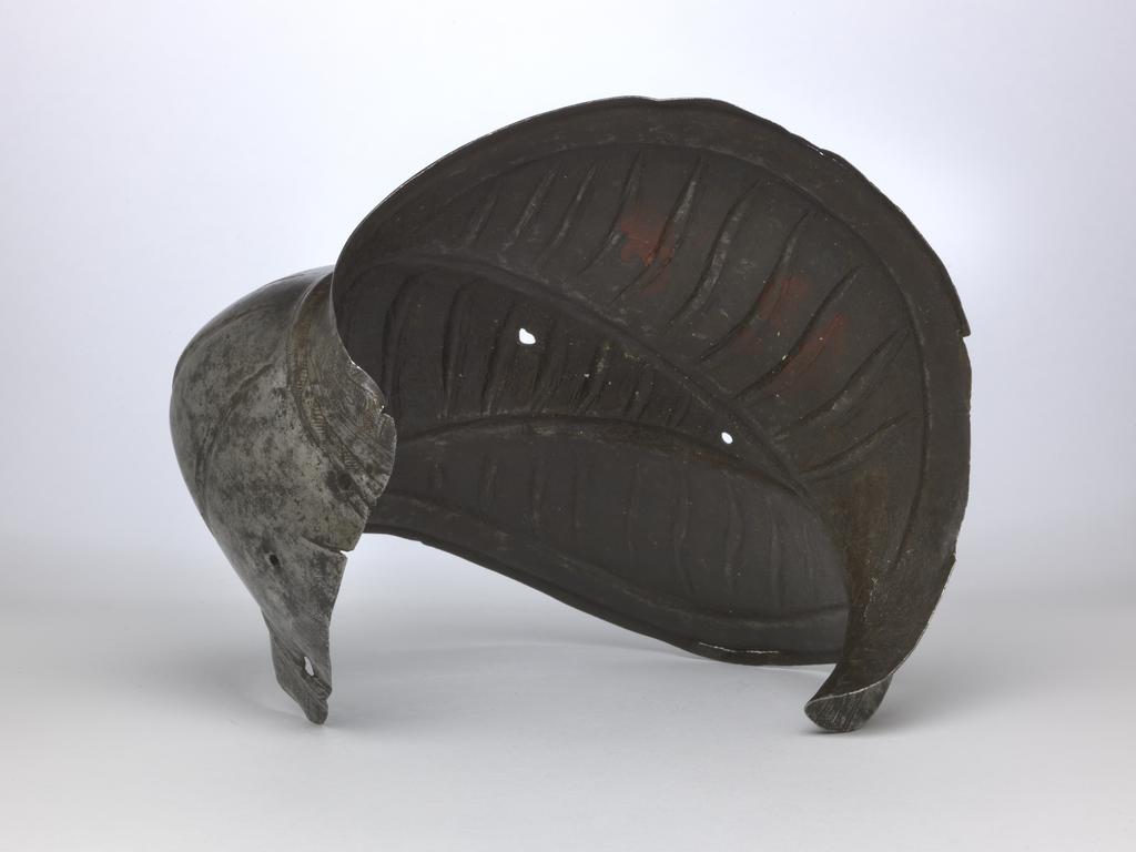 An image of Armour. Couter for the right elbow, for parade use, with 'puffed-and-slashed' decoration in imitation of civilian costume. Unknown production, South Germany. Formed of a single, shell-like plate, open at the rear and strongly shaped to the point of the elbow. Its outer edge is straight. Its upper and lower edges are convex and converge at the inside of the elbow in a strong, medial pucker. The upper and lower edges have partial inward turns accompanied by recessed borders decorated with etched and gilt tulip-like flower heads on a cross-hatched ground separated by broad bands enclosed by pairs of narrower bands. The boss over the elbow is enclosed by a pair of raised ribs that converge to the inside of the elbow. Each rib is decorated with etched diagonal bands that are alternatively hatched and gilt, and plain. The remainder of the couter, with the exception of its inner and outer ends is decorated with slender, vertical, recessed 'slashes' in imitation of those found on contemporary costume. The slashes on the upper and lower wings are slightly recurved, while those on the central boss are curved or straight. The front and rear of the central boss are each pierced with a rivet-hole for the attachment of the missing pair of vertical internal leathers that formerly connected the couter to the upper and lower cannons of the vambrace. The outer end of the couter is pierced with a pair of widely-spaced rivet-holes for the attachment of a missing bifurcated strap that terminated in a buckle to receive the missing strap that was formerly attached by a rivet occupying a now vacant hole located just to the inside of the medial pucker, and passed around the rear of the elbow. The couter is bright, with patches of dark patination. Its upper and lower edges both exhibit cracks. A small section at the inner end of the lower edge has broken away. The outer edge of the couter has a crack just below its centre, and its lower corner is bent inwards. Hhammered, shaped, riveted, wit
