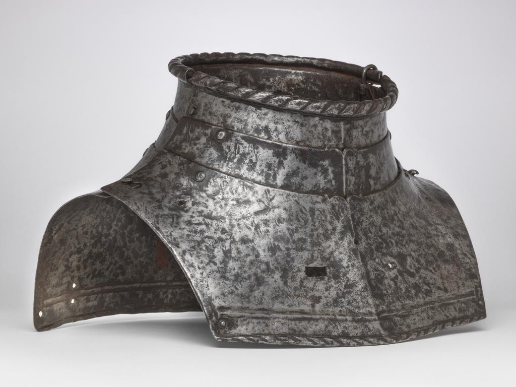 An image of Armour. 'Almain' collar, for light field use, lacking its integral spaudlers. Unknown production, Germany. Formed of three upward-overlapping lames front and rear. The front lames are medially ridged. The upper edges of the second and third front lames are each decorated at their centres with a filed ogee. The upper edge of the top lame at both the front and rear has a boldly roped inward turn. The bottom lame in each instance is considerably deeper than the rest. The lower edge has a roped inward turn accompanied by a recessed border and an enclosing raised rib. The lower edge of the front lame is obtusely pointed while the lower edge of the rear lame is almost straight. The lames were originally connected to one another by three lames front and rear. Each leather was retained by single rivets which were externally flush on the first and second lames and round-headed with internal washers on the third lame. Construction-holes aligning with the rivet-holes for the outer leathers of the second and third lames were originally filled with purely decorative round-headed rivets. These construction-holes and the underlying leathering-holes are now filled by modern round-headed rivets that secure the lames directly to one another at their outer ends. The unused outer leathering-holes on the fourth lame now remain vacant, as do all the central leathering-holes. The central hole in the first rear lame has been modified to a vertical slot which has broken out to the lower edge of the lame. A later hole located just to the right of the slot is plugged with an externally-flush rivet. The front and rear sections of the collar are connected to one another at the top of the left side by means of an integral hinge cut out of the ends of the first lames. The inward-folded ends of the hinge are each secured by an externally-flush rivet. That in the rear lame has lost its head. The pivot of the hinge has been replaced by a long piece of wire bent over the top edge of the collar. The f