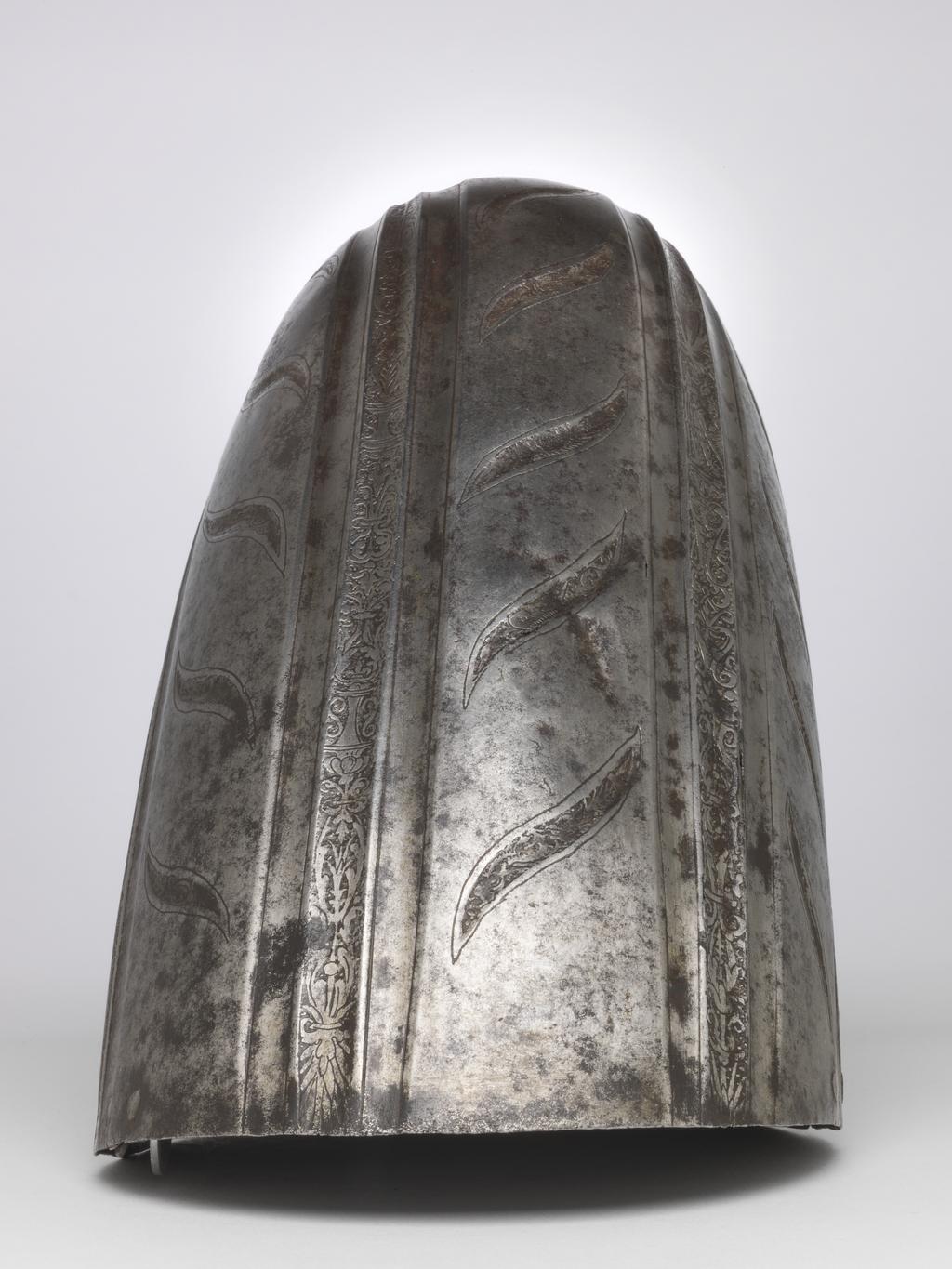 An image of Armour. Couter and lower cannon of a vambrace for the right arm, for parade use, with 'puffed-and-slashed' decoration in imitation of civilian costume. Production Place: South Germany. Helmschmied, Koloman (German, 1470/71-1532). The couter is formed of a single, large, shell-like plate, open at the rear and strongly shaped to the point of the elbow. Its outer edge is nearly straight. Its upper and lower edges are convex and converge at the inside of the elbow in a strong, medial pucker. The upper and lower edges have inward turns, roped with pairs of incised lines. The turns are each accompanied by a recessed border which is itself accompanied on the front by a flute separated from the border by a raised rib emphasised by a pair of incised lines. The boss over the elbow is enclosed by two groups of three flutes, each emphasised by pairs of incised lines, that converge to the inside of the elbow. Two vertical groups of such flutes decorate the front of the couter both above and below the boss, while three more decorate the boss itself. The broad bands intervening between these groups of flutes are decorated with slender, diagonal, slightly recurved, recessed 'slashes' in imitation of those found on contemporary civilian costume. The front and rear of the central boss are each fitted with a pair of horizontally-aligned rivets for the attachment of a missing pair of vertical internal leathers that formerly connected the couter to the upper and lower cannons of the vambrace. The outer end of the couter is filled with a pair of widely-spaced, externally-flush rivets for the attachment of a missing bifurcated strap that terminated in a buckle to receive the missing strap that was formerly retained internally by a brass-capped, round-headed rivet and octagonal internal washer located just to the inside of the medial pucker, and passed around the rear of the elbow. The lower cannon is of tubular form, cut away in a concave curve towards the inside of the elbow, and constri