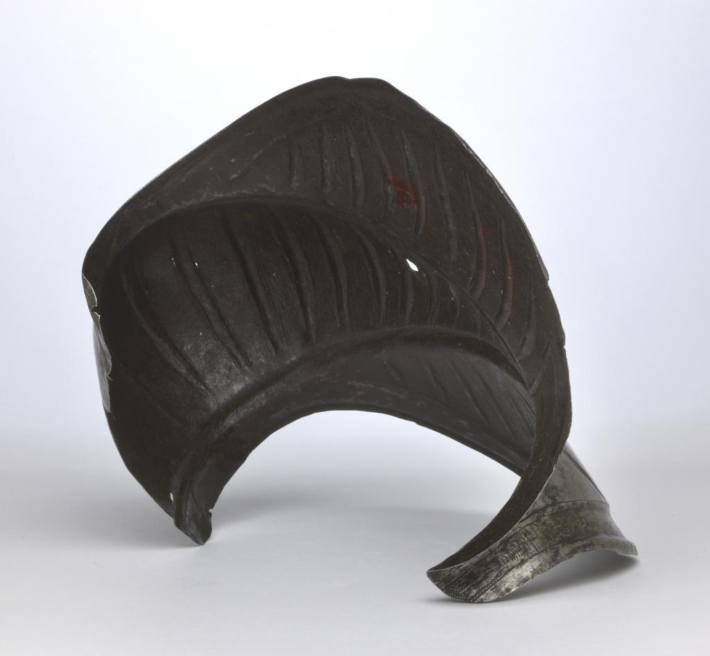 An image of Armour. Couter for the right elbow, for parade use, with 'puffed-and-slashed' decoration in imitation of civilian costume. Unknown production, South Germany. Formed of a single, shell-like plate, open at the rear and strongly shaped to the point of the elbow. Its outer edge is straight. Its upper and lower edges are convex and converge at the inside of the elbow in a strong, medial pucker. The upper and lower edges have partial inward turns accompanied by recessed borders decorated with etched and gilt tulip-like flower heads on a cross-hatched ground separated by broad bands enclosed by pairs of narrower bands. The boss over the elbow is enclosed by a pair of raised ribs that converge to the inside of the elbow. Each rib is decorated with etched diagonal bands that are alternatively hatched and gilt, and plain. The remainder of the couter, with the exception of its inner and outer ends is decorated with slender, vertical, recessed 'slashes' in imitation of those found on contemporary costume. The slashes on the upper and lower wings are slightly recurved, while those on the central boss are curved or straight. The front and rear of the central boss are each pierced with a rivet-hole for the attachment of the missing pair of vertical internal leathers that formerly connected the couter to the upper and lower cannons of the vambrace. The outer end of the couter is pierced with a pair of widely-spaced rivet-holes for the attachment of a missing bifurcated strap that terminated in a buckle to receive the missing strap that was formerly attached by a rivet occupying a now vacant hole located just to the inside of the medial pucker, and passed around the rear of the elbow. The couter is bright, with patches of dark patination. Its upper and lower edges both exhibit cracks. A small section at the inner end of the lower edge has broken away. The outer edge of the couter has a crack just below its centre, and its lower corner is bent inwards. Hhammered, shaped, riveted, wit
