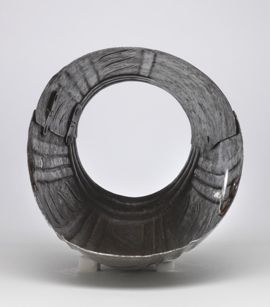 An image of Armour. Couter and lower cannon of a vambrace for the right arm, for parade use, with 'puffed-and-slashed' decoration in imitation of civilian costume. Production Place: South Germany. Helmschmied, Koloman (German, 1470/71-1532). The couter is formed of a single, large, shell-like plate, open at the rear and strongly shaped to the point of the elbow. Its outer edge is nearly straight. Its upper and lower edges are convex and converge at the inside of the elbow in a strong, medial pucker. The upper and lower edges have inward turns, roped with pairs of incised lines. The turns are each accompanied by a recessed border which is itself accompanied on the front by a flute separated from the border by a raised rib emphasised by a pair of incised lines. The boss over the elbow is enclosed by two groups of three flutes, each emphasised by pairs of incised lines, that converge to the inside of the elbow. Two vertical groups of such flutes decorate the front of the couter both above and below the boss, while three more decorate the boss itself. The broad bands intervening between these groups of flutes are decorated with slender, diagonal, slightly recurved, recessed 'slashes' in imitation of those found on contemporary civilian costume. The front and rear of the central boss are each fitted with a pair of horizontally-aligned rivets for the attachment of a missing pair of vertical internal leathers that formerly connected the couter to the upper and lower cannons of the vambrace. The outer end of the couter is filled with a pair of widely-spaced, externally-flush rivets for the attachment of a missing bifurcated strap that terminated in a buckle to receive the missing strap that was formerly retained internally by a brass-capped, round-headed rivet and octagonal internal washer located just to the inside of the medial pucker, and passed around the rear of the elbow. The lower cannon is of tubular form, cut away in a concave curve towards the inside of the elbow, and constri