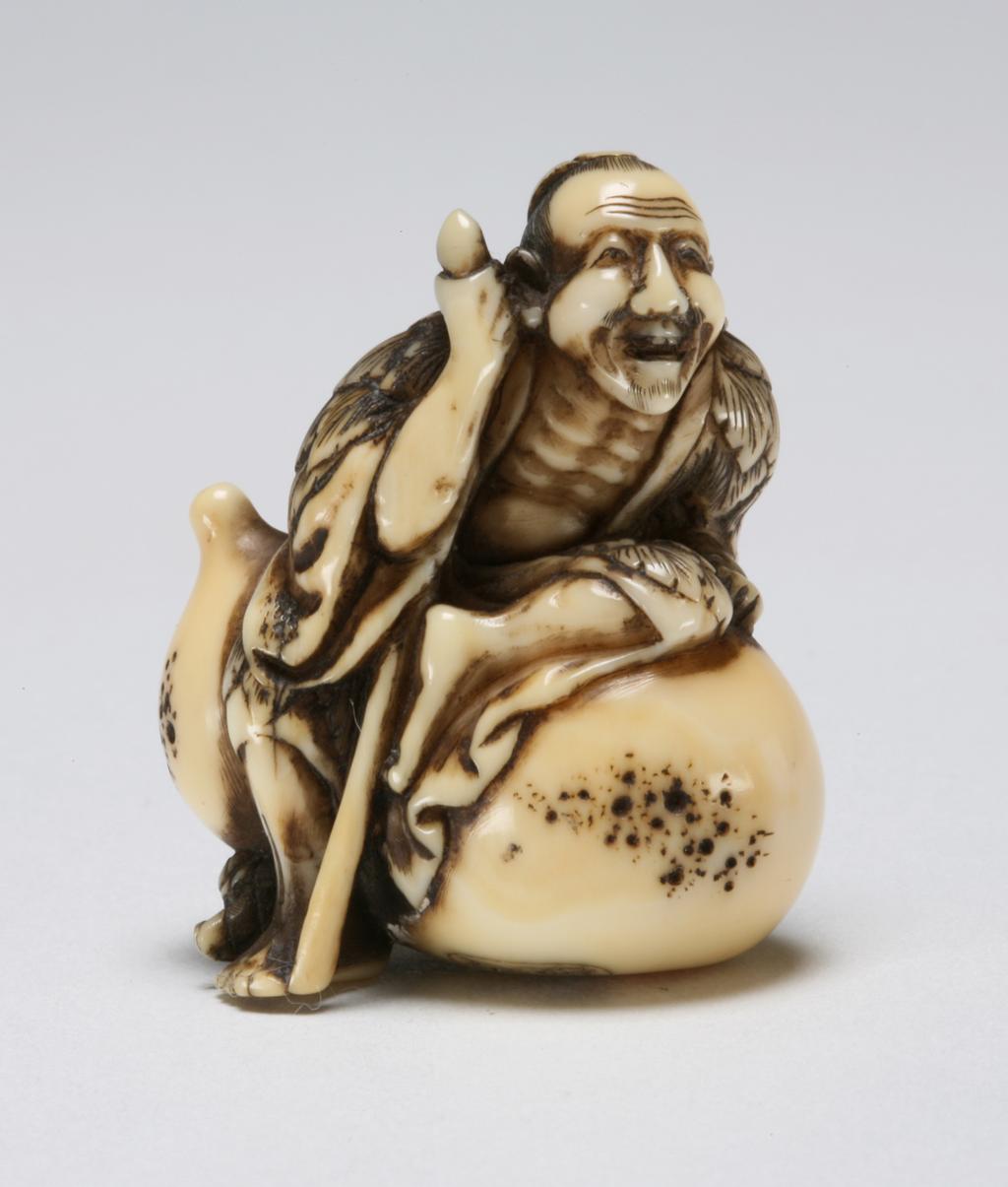 An image of Netsuke: katabori: Sennin Tekkai. Chogetsu, Edo Period (1603-1868). Figure of Sennin Tekkai as an old beggar holding a staff in his right hand, barefoot and wearing a cloak made of leaves revealing his ribs, blowing his spirit into space through his open mouth. He is seated on a gourd. The details are finely carved and incised. Himotoshi on the underside. Ivory, carved, incised and stained, height, whole, 4.0 cm, width, whole, 3.5 cm, circa 1800-1868. Edo Period (1615-1868).