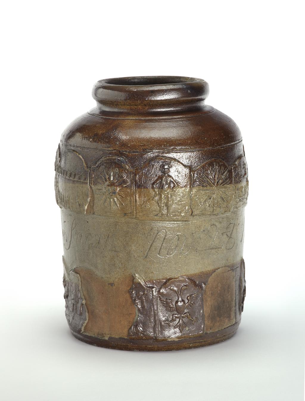 An image of Pickle jar. Unidentified pottery, possibly London. The jar is cylindrical with curved shoulders, a short incurved neck and rolled mouth. Round the middle are incised the names and date 'George Bennison & Sarah Nov 28 1752', Above and below this, there is a band of adjacent inn-signs. Above: The Four Swans, The Grenadier, The Crown, The King's Head (with initials GR), the Duke of Marlborough (DM), The Peal of Bells (eight bells and bell ringers), The Sun, The Jolly Sailor, The Star, The Hart, and The Noah's Ark. Below: The Bull, The Griffin, The Bell, The Swan, The Rose (with the name Wm Hasmere?), The Castle (? part missing), The Angel, The Spread Eagle, another missing, and The Angler (?). Greyish buff stoneware, thrown, decorated with applied moulded reliefs, coated with dark brown dip on the upper and lower part of the sides, and salt-glazed, height, whole, 27.3 cm, dated 1752.