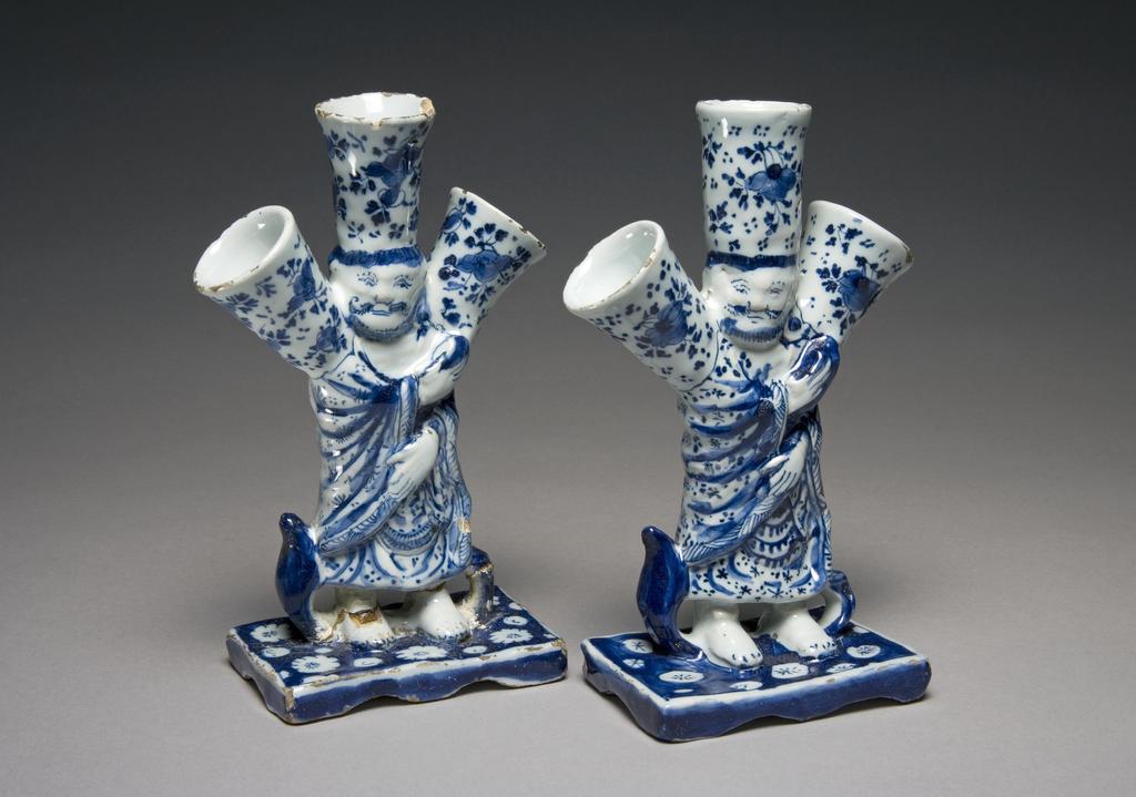 An image of Description: 2 Flower vases in the form of a Chinese sage or deity with three spouts for flowers on his head and shoulders, of tin-glazed earthenware painted in blue
Production Place: Delft (factory), United Provinces of the Netherlands (country) 
Dimensions:  height (Both): (whole): 18 cm
Date: circa 1700 to 1725 
 
  
 