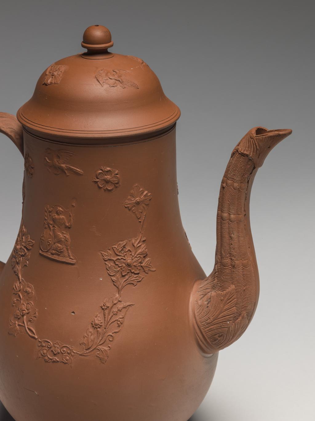An image of Coffee pot and cover. Unknown Staffordshire factory. The body thrown, with applied moulded handle and spout, and mould applied sprigging. The pot is pear-shaped with a long curved spout moulded with wicker pattern and foliage, and a loop handle. One side is decorated with a mould-applied figure of Britannia with lion and Union Jack shield, on which is the number '45'; on the other side there is a grotesque Chinese figure seated under a parasol. Above both figures there is a flying bird, and below a festoon of mould applied stylized flowers and scrollwork. The domed cover is decorated with a similar bird and flowers, and has an acorn-shaped knob. Red dry-bodied stoneware, circa 1763-1765. Rococo.