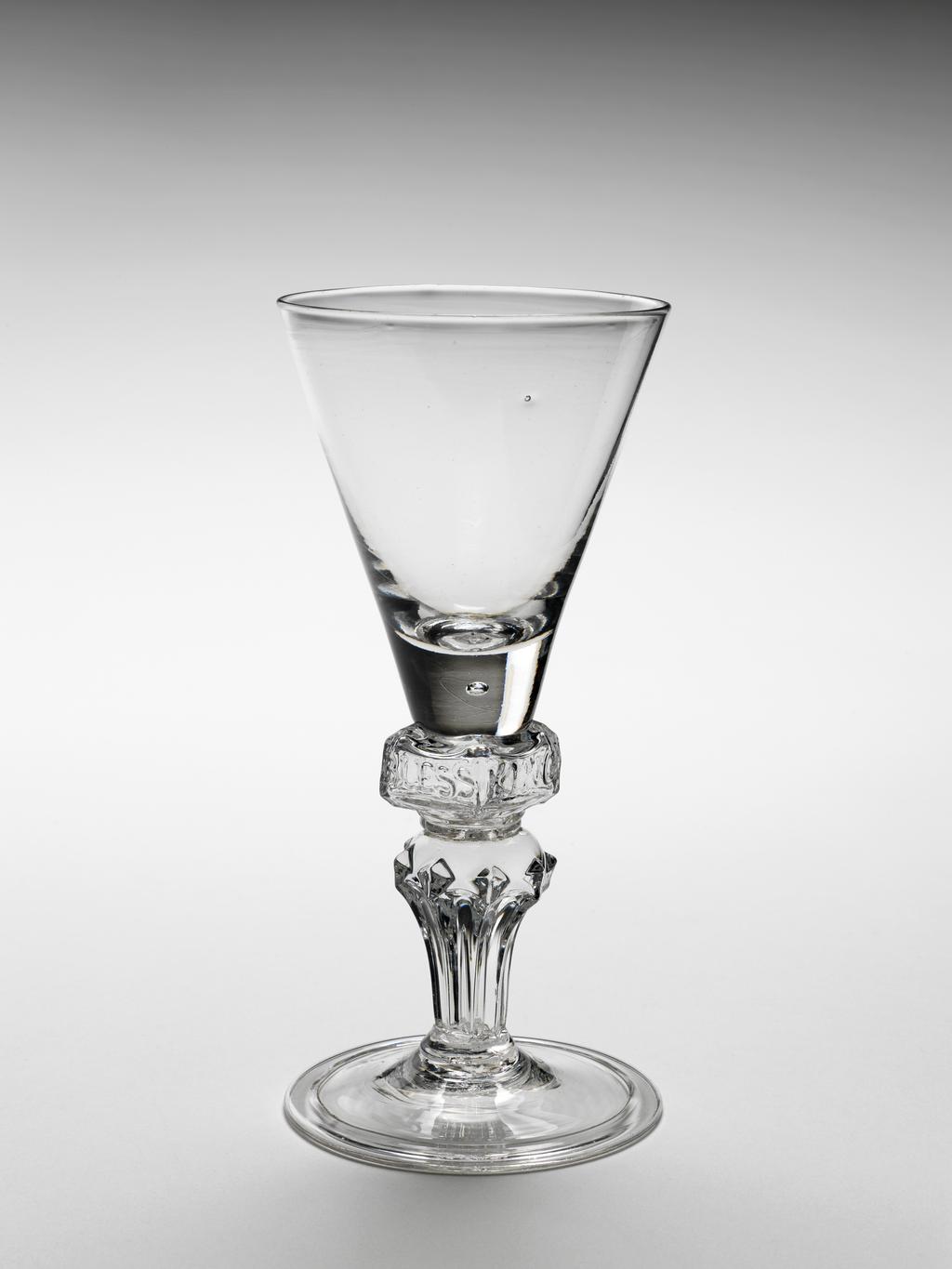 An image of Wine glass. Funnel bowl on square knop moulded 'GOD SAVE KING GEORGE' on moulded pedestal stem and folded foot. Lead glass, bowl blown, stem moulded with engraved decoration, height 16.0cm, diameter (whole) 7.5cm, circa 1715.
