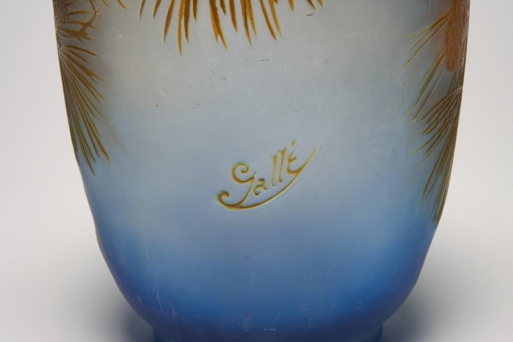 An image of Gallé, Emile (French, 1846-1904.) Glass vase cut with an assymetrical design of pine branches and cones. Blue blown glass, cased in orange and brown, and carved, height 27.0cm, diameter (whole) 16.6cm, circa 1890. French.