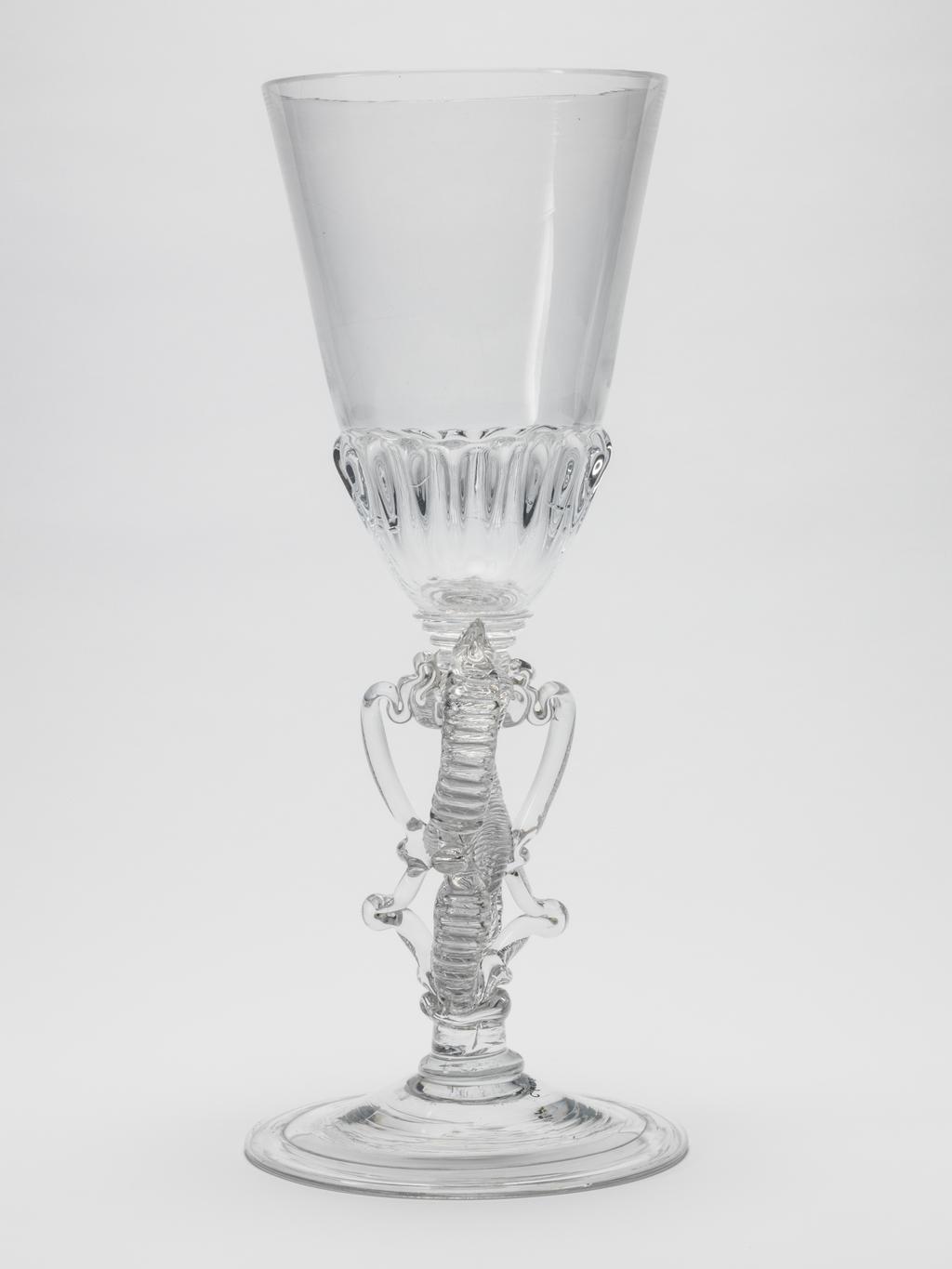 An image of Ceremonial goblet/drinking glasses. Unknown glassmaker. Heavy, moulded gadrooning on base of bowl and on cover; figure-of-eight stem; folded foot; cover finial composed of trailed and dentilated scrolls to either side of a tall spire constructed of a series of knops. Clear lead-glass, bowl blown, height, goblet, 37.5 cm, diameter, goblet, 15.5 cm, height, cover, 14.4 cm, diameter, cover, 15.4 cm, circa 1713.