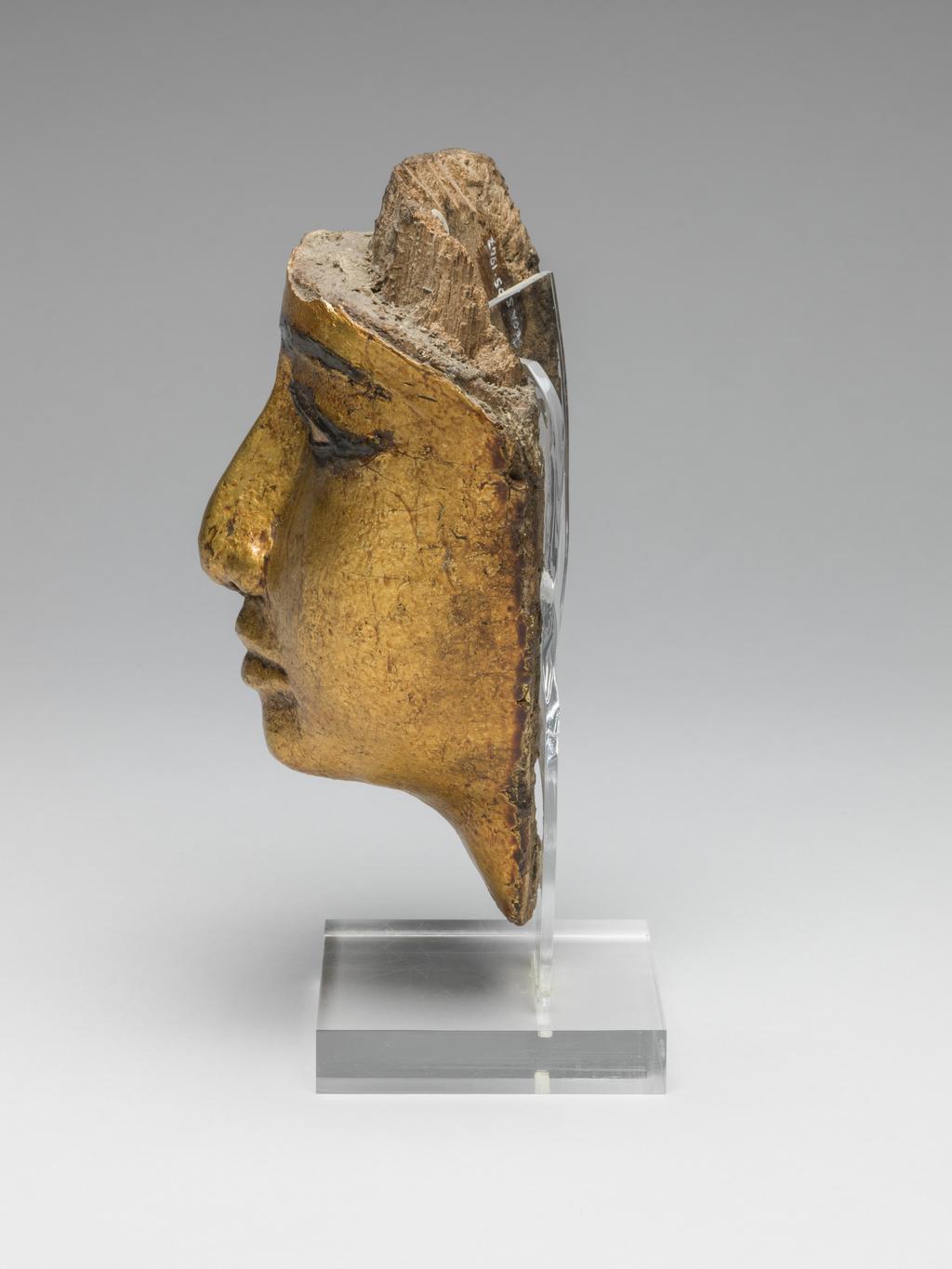 An image of Funerary Equipment/Coffin. Face from coffin, with eyes and eyebrows inlaid, gilded. Production Place/Find Spot: Egypt. Wood (gilded), carved, depth 7.5 cm, length 16.6 cm, width 11.9 cm, 1186-1069 B.C. Twentieth Dynasty, New Kingdom.