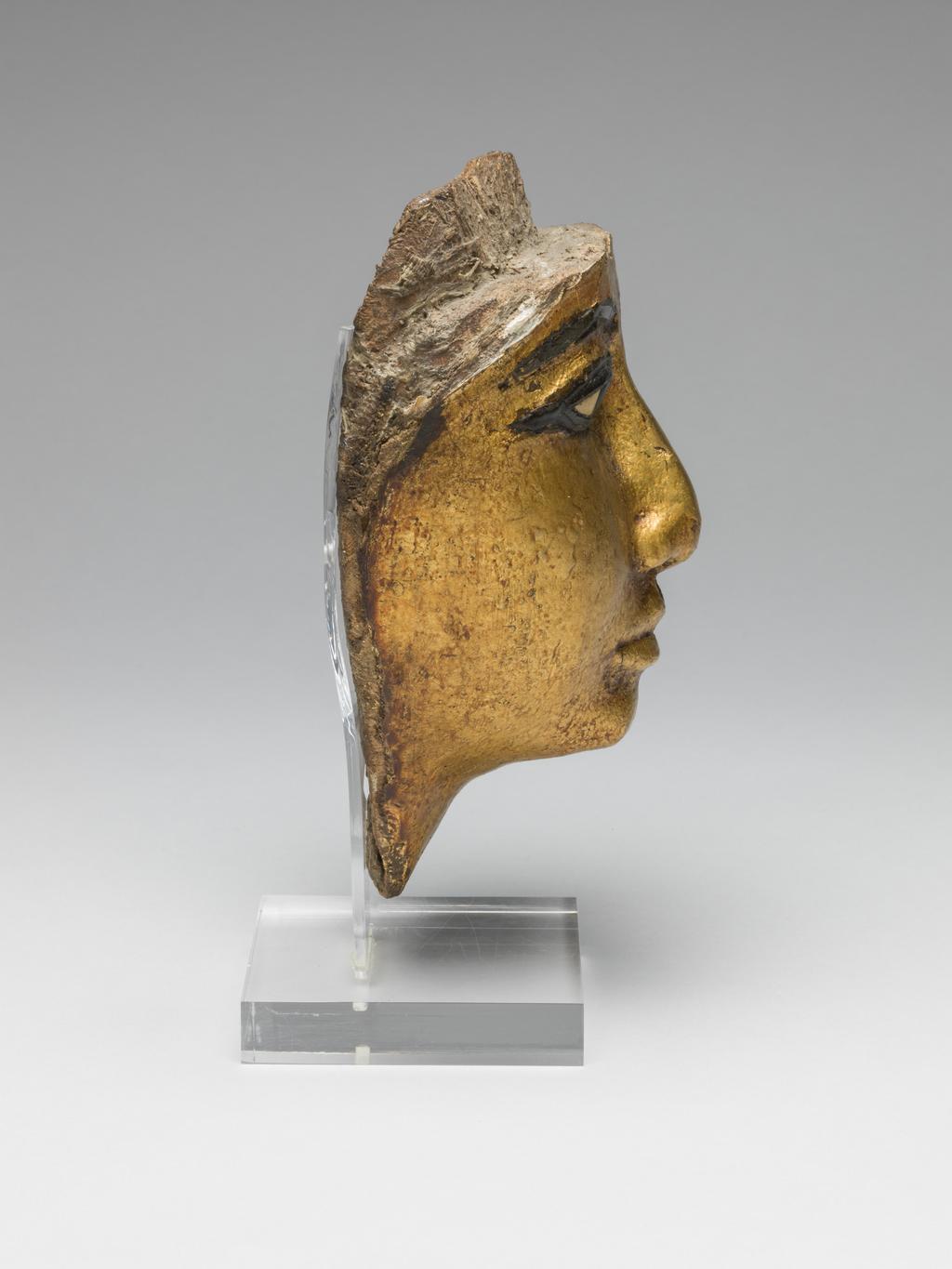 An image of Funerary Equipment/Coffin. Face from coffin, with eyes and eyebrows inlaid, gilded. Production Place/Find Spot: Egypt. Wood (gilded), carved, depth 7.5 cm, length 16.6 cm, width 11.9 cm, 1186-1069 B.C. Twentieth Dynasty, New Kingdom.