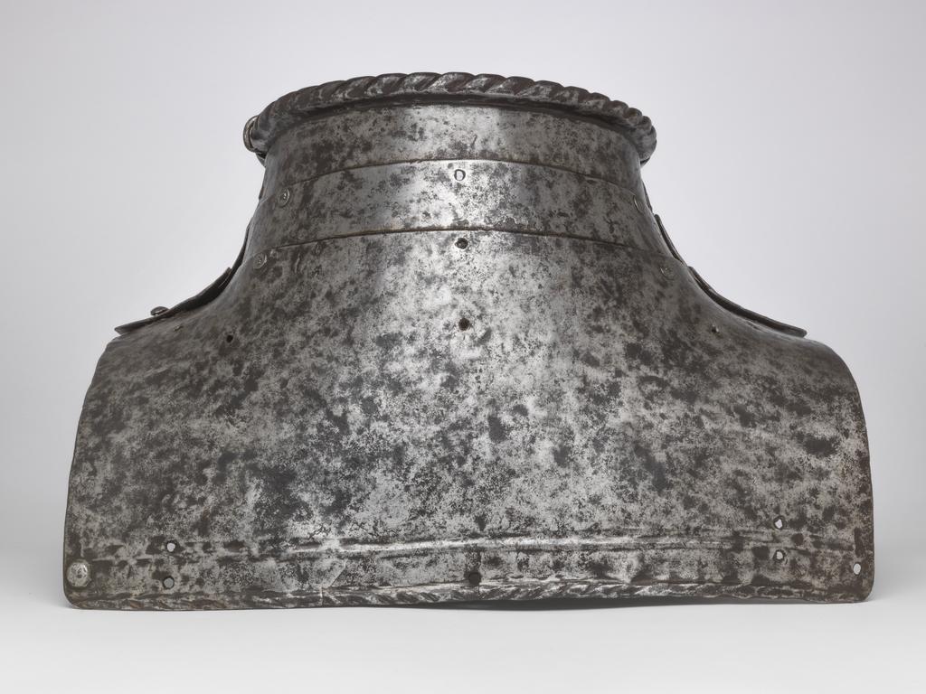 An image of Armour. 'Almain' collar, for light field use, lacking its integral spaudlers. Unknown production, Germany. Formed of three upward-overlapping lames front and rear. The front lames are medially ridged. The upper edges of the second and third front lames are each decorated at their centres with a filed ogee. The upper edge of the top lame at both the front and rear has a boldly roped inward turn. The bottom lame in each instance is considerably deeper than the rest. The lower edge has a roped inward turn accompanied by a recessed border and an enclosing raised rib. The lower edge of the front lame is obtusely pointed while the lower edge of the rear lame is almost straight. The lames were originally connected to one another by three lames front and rear. Each leather was retained by single rivets which were externally flush on the first and second lames and round-headed with internal washers on the third lame. Construction-holes aligning with the rivet-holes for the outer leathers of the second and third lames were originally filled with purely decorative round-headed rivets. These construction-holes and the underlying leathering-holes are now filled by modern round-headed rivets that secure the lames directly to one another at their outer ends. The unused outer leathering-holes on the fourth lame now remain vacant, as do all the central leathering-holes. The central hole in the first rear lame has been modified to a vertical slot which has broken out to the lower edge of the lame. A later hole located just to the right of the slot is plugged with an externally-flush rivet. The front and rear sections of the collar are connected to one another at the top of the left side by means of an integral hinge cut out of the ends of the first lames. The inward-folded ends of the hinge are each secured by an externally-flush rivet. That in the rear lame has lost its head. The pivot of the hinge has been replaced by a long piece of wire bent over the top edge of the collar. The f