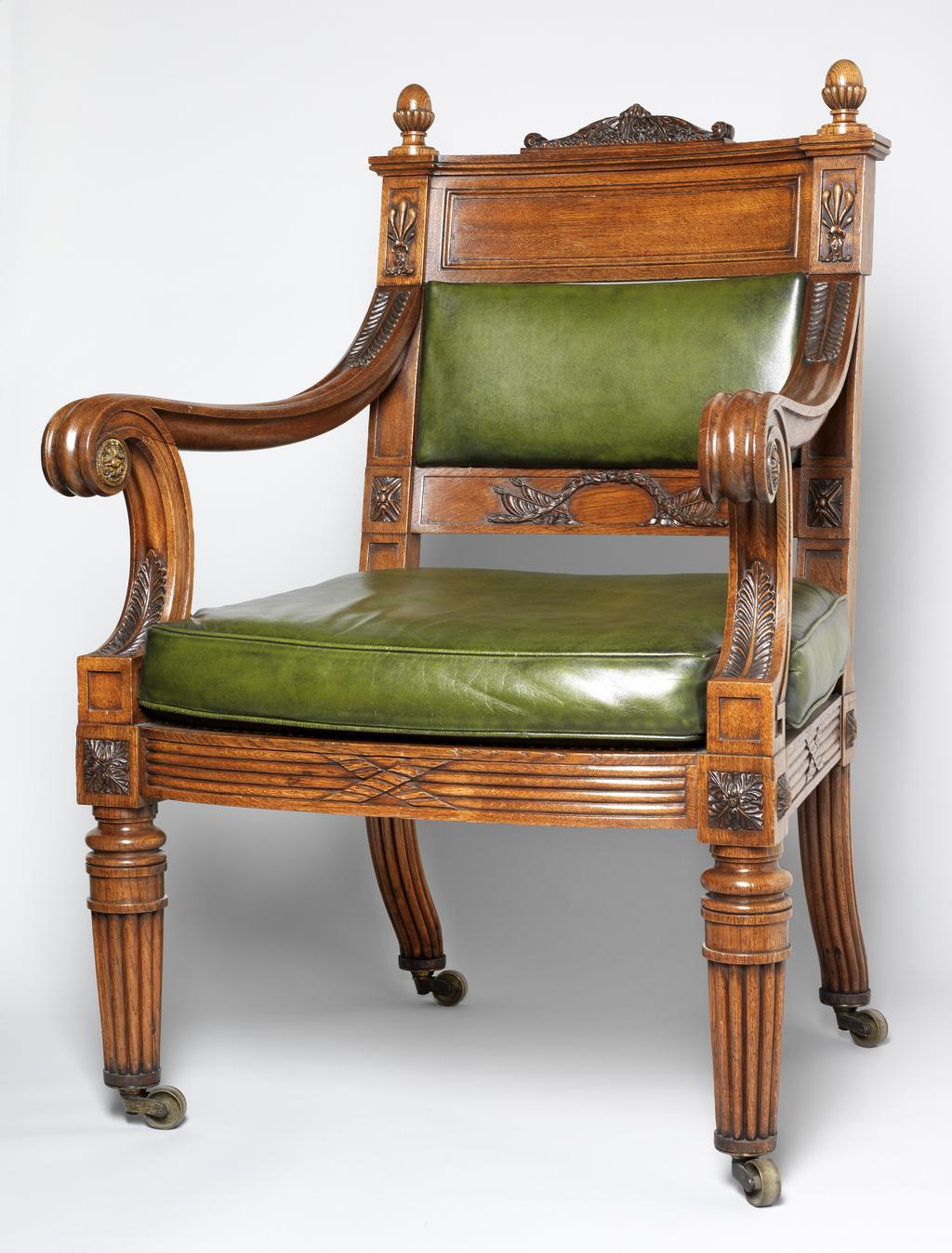 An image of Furniture. Chippendale, Thomas II, attributed to (British, 1749-1822). Armchair of carved oak with turned legs and caned seat, with modern green leather squab seat cushion and back panel and brass casters. Replacement back and cushions, Old woodworm holes. Oak frame, cane seat, leather back panel, cushion (replacement), brass (alloy) castors, height, 107.5 cm, width, front, 68 cm, width, back, 57 cm, depth, 64.2 cm, circa 1820 to circa 1821. Regency Period. Production Note: The design is related to three chairs carved from the famous 'Waterloo Elm'. Two were commissioned from Thomas Chippendale by John George Children (1777-1852). The first was given to George IV in 1821 at Carlton House, and is now at Windsor Castle. The second was for Children's own use. It was given by him to the Duke of Wellington in 1837, and now at Apsley House, London. A third armchair was commissioned by the Duke of Rutland, and is at Belvoir Castle. The Fitzwilliam's chair is close in design to the chair at Apsley House.