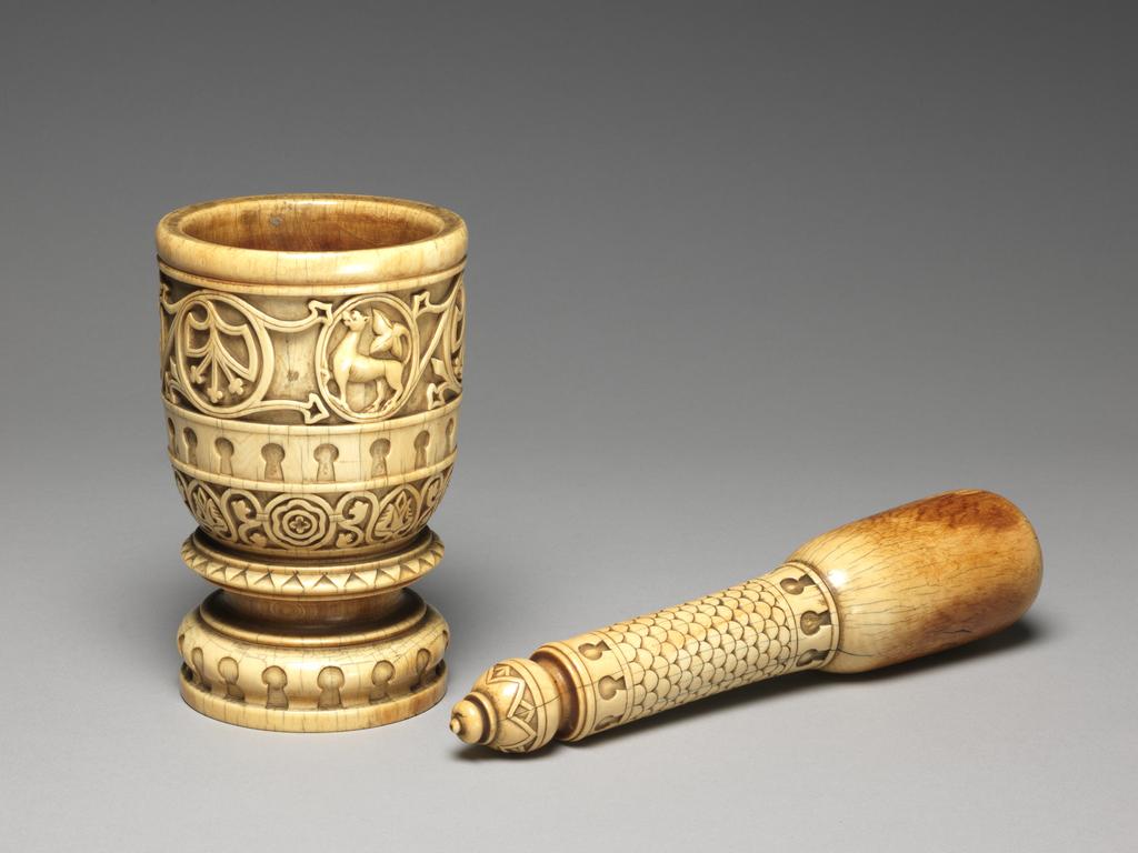 An image of Sculpture/ Pestle and mortar. The mortar is decorated with bands of ornament: a) at the top: a plain rim; b) a band of stylised foliated scroll-work with three medallions, each containing a fabulous beast with a foliated tail: c) a band of key-hole ornament; d) a band of stylised foliated scroll-work with four medallions, each containing a rosette. Around the thick short stem the mortar has several mouldings, including another band of key-hole pattern.The pestle handle is decorated with a scale pattern with a band (at the top and bottom) of key-hole pattern. A bulbous knob terminates the handle, and is carved with a triangular pattern. Ivory elaborately carved, height, pestle, 8.0 in, height, mortar, 5 1/4 in, diameter, mortar at top, 2 3/4 in, diameter, mortar at bottom, 2 7/8 in. Circa 1700-1800. Production Place: Sicily.