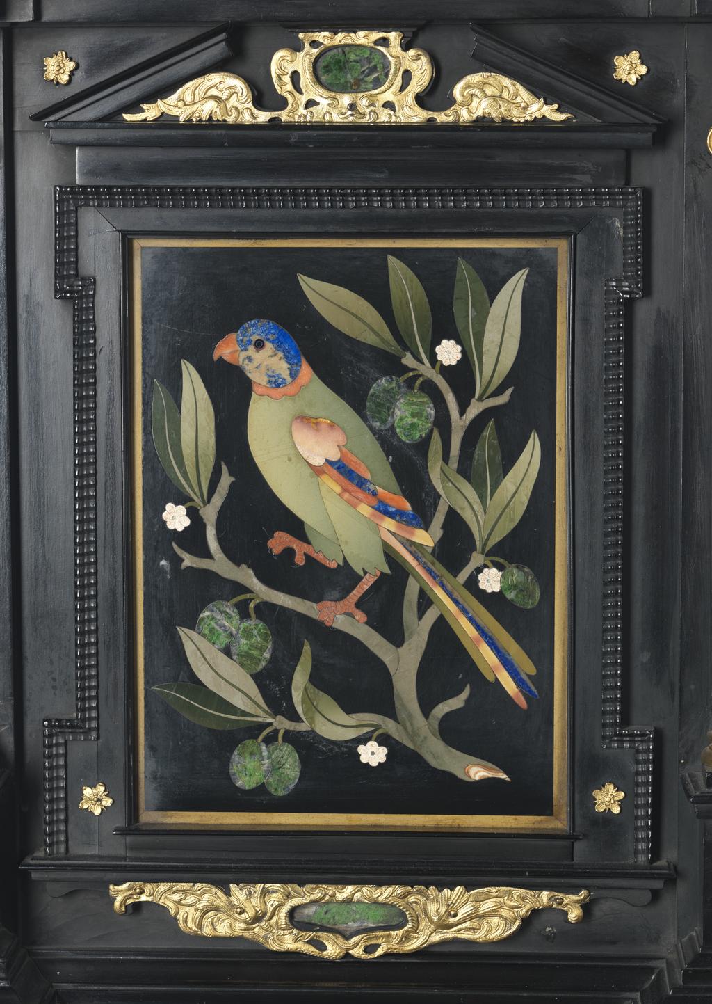 An image of Augsburg 17th century silver-gilt mounted ebony Table Cabinet with Florentine pietre dure plaques from the Grand Ducal workshops. Boscher, Elias (1600-1674). Of architectural form, the stepped superstructure fitted with three frieze drawers above a central cupboard door, architectural pediment and inset with a panel depicting a chaffinch on a fruiting bough, flanked by columns of Smaragdite Gabbro with Corinthian capitals flanked by two deep drawers, inset with panels depicting parrots within fruiting boughs, with three further fitted drawers below, the large central cupboard door inset with a panel of a lapis lazuli flower filled urn issuing stems including a carnation, anemone, daffodil and lilies and enclosing an architectural interior, flanked by further Smaragdite Gabbro Ionic columns and three drawers to each side inset with further symmetrical floral panels including tulips, roses, carnations, lilies and bluebells, on shaped bracket feet, each side inset with large central panels of parrots on fruiting boughs, with four further floral panels above and below, the reverse veneered in kingwood, amaranth and stained walnut in geometric stellar designs. The cabinet containing a complex series of fourty-four secret drawers and compartments to the interior. The cabinet is signed in pencil on the underside 'Elias Boscher' and 'gemacht'. The central cabochon mount stamped with the Augsburg town mark and the silversmiths mark of Johann Spitzmacher (active 1655-1678). The front bears the ebony stamp "EBEN" with the pinecone of Augsburg. Height 85 cm, width 84cm, depth 40cm, circa 1660.