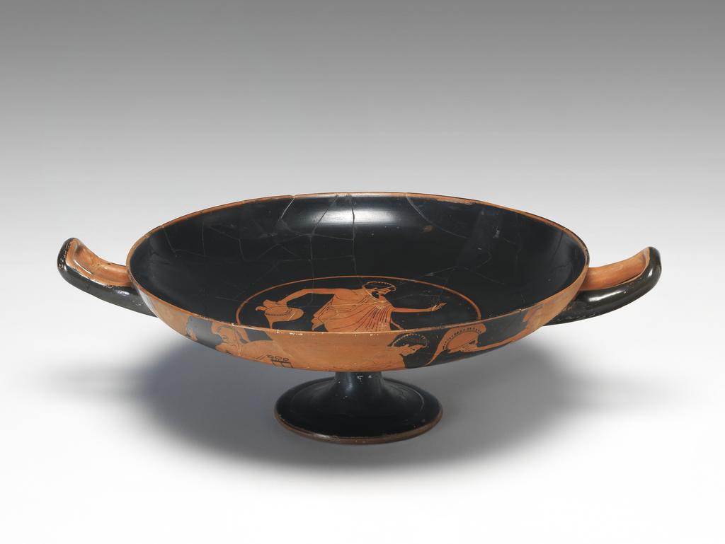 An image of Vessel/Cup. Painter of Berlin 2268 (vase-painter, ca. 530-500 BC). (A,B) warriors and draped youths, one with flower, snake, dog, tripod (I) draped man with staff. Production Place: Athens. Find Spot: Vulci Etruria Italy. Red figured, clay, diameter, 0.273 m, height 0.106 m, width 0.351 m, diameter, 0.146 m. 500-490 B.C. Archaic Period.