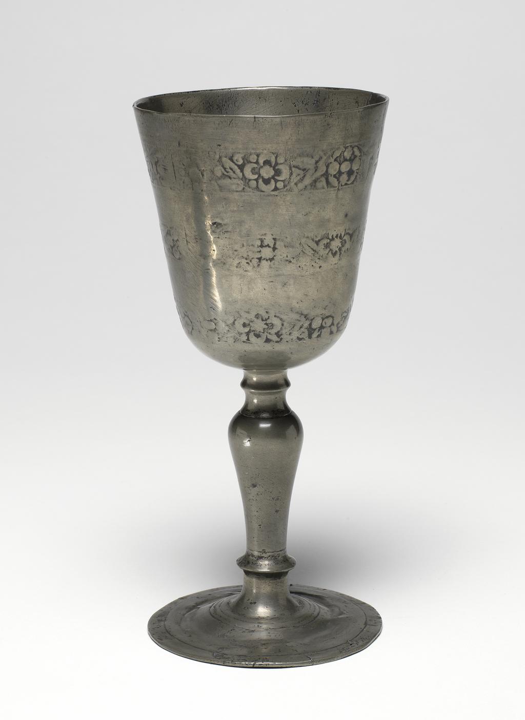 An image of Chalice. Pewter with relief decoration. The rounded conical bowl has three bands of floral motifs and is supported on a baluster stem and circular foot. Height (whole) 17.6 cm, diameter (rim) 8.2 cm, circa 1600 to 1620. English.