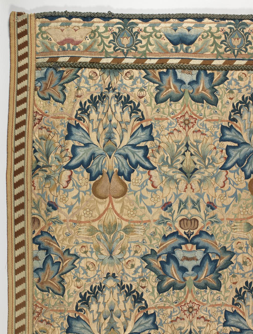 An image of Textile. Wall Hanging. Morris, William, designer (British, 1834-1896), Godman, Ada Phoebe, embroiderer (British. Wall hanging, of linen, with polychrome wool embroidery in 'Artichoke' pattern. Linen twill, embroidered in crewel wools in shades of cream, beige, pale, medium and dark brown, yellowish-brown, pale yellow, salmon pink, pale, medium and dark rose pink, pale, medium and dark green, pale medium and dark Prussian blue, pale blue, grey, and white with Artichoke design incorporating stylized artichokes, other flowers, and foliage. The borders are of oblique stripes, and the lower edge is fringed. Height (whole) 213.5 cm, width (whole) 983.6 cm, circa 1875-circa 1899. Arts and Crafts. Notes: The design of 1877 entitled 'Mrs Godman. Design for embroidered hanging (artichoke design)' is in the Victoria & Albert Museum (65-1898). This hanging and the other pieces which covered the walls of the room were worked by Mrs Godman over about twenty-five years.