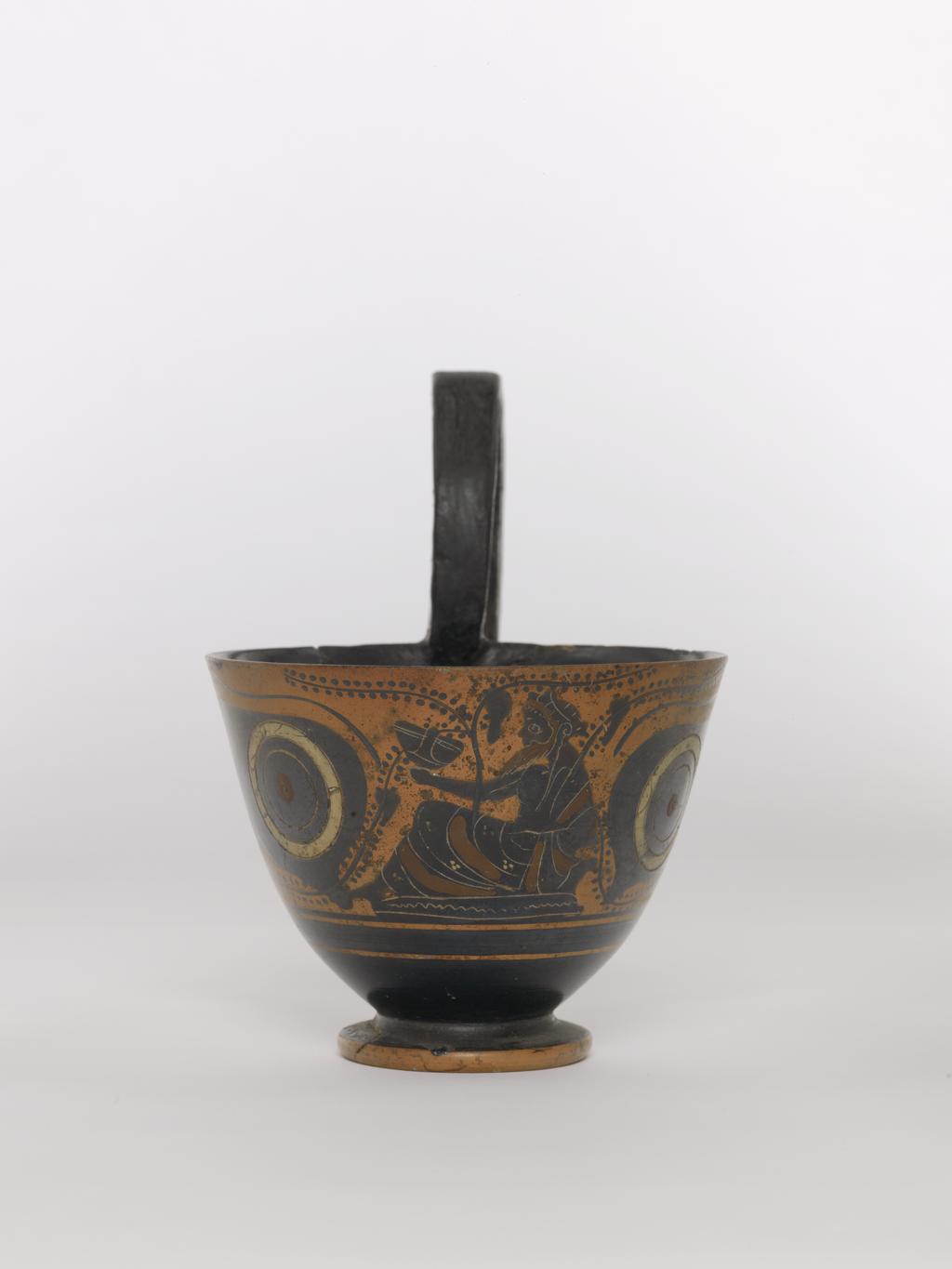 An image of Vessel. Kyathos, Dionysos and lions. Production Place: Athens, Attica, Greece. Clay, black-figured, height 0.076 m, diameter, rim, 0.099 m, diameter, base, 0.049 m, height 0.131 m, 500 B.C. Archaic Period.