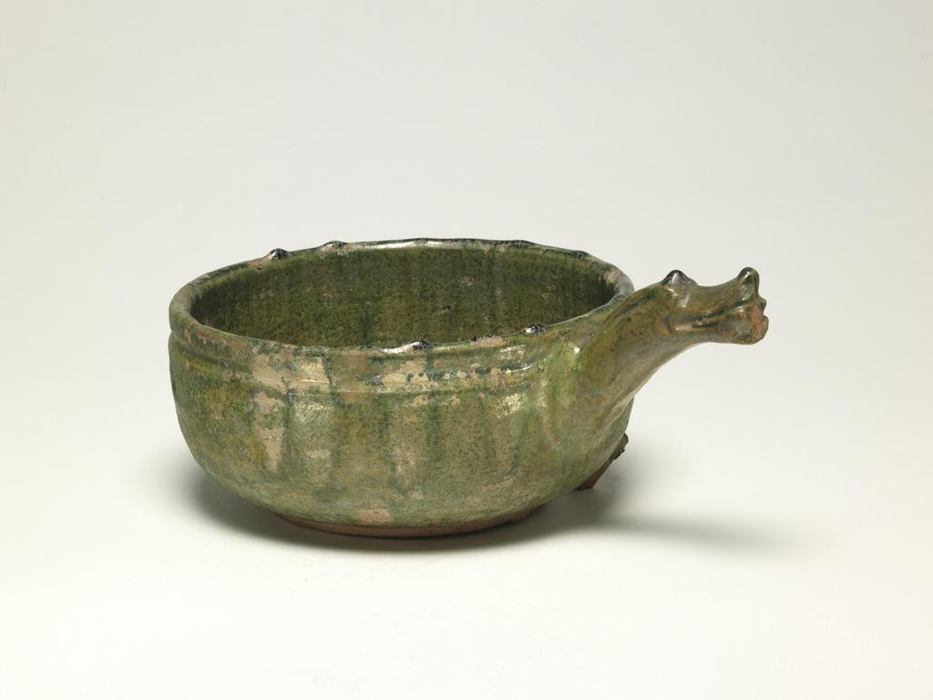 An image of Bowl shaped earthenware cooking vessel with an animal headed handle. The vessel is covered in a yellow green glaze, except for the sculptured ring foot with a slightly concaved base. Very fine terracotta coloured biscuit. Chips are missing from the mouth rim and body. Broken spurs (from other vessels during the firing process) adher to the lower body. Earthenware, glazed, height 8.5 cm, diameter 16.5 cm. Han Dynasty (BC 206 - AD 220). Chinese.