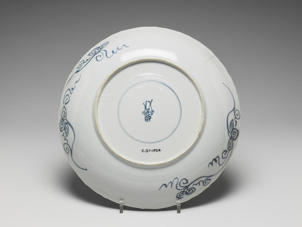 An image of Plate. Unknown production, China. The plate is painted in underglaze blue, decorated with asters in petal-shaped panels at the border enclosing five similar flower-heads amongst a dense whorled-pattern at the centre. On the base there are two encircled fish with a flower. This design was especially popular in the Middle East. Hard-paste porcelain, underglaze colour, height 3.9 cm, diameter 27.2 cm, 1600-1699.