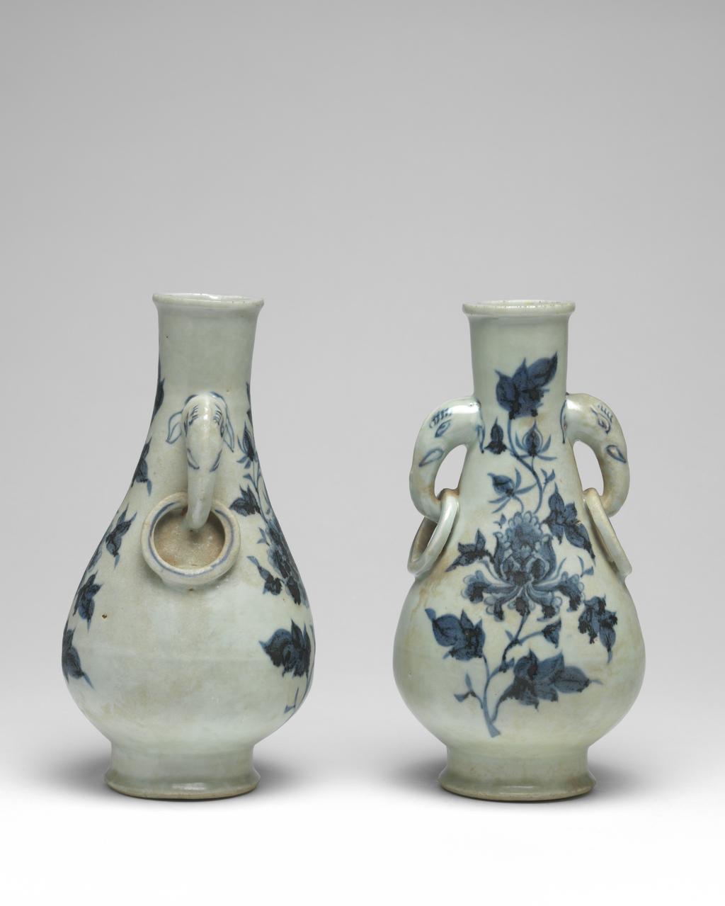 An image of Vase with elephant handles. Unknown maker, China, Folk kilns. The pear-shaped vase has a slender neck, thick, rounded lip, and two elephant head and fixed-ring handles. The body tapers to a deep, flared foot with deep flat, recessed base. The elephant handles are finely painted with eyes, eyelashes, tusks and ears, and the fixed rings with single circle ornament. On each side of the body are elegant peony sprays in blue. The interior is unglazed, as is the base which is covered with a red, sandy deposit. Hard-paste porcelain, thrown, painted in underglaze blue, with base and interior unglazed. Height, whole, 24.6 cm, diameter, whole, 12.7 cm, circa 1300-1368. Yuan Dynasty (1206-1368). Collection: H.S. Reitlinger. Of a pair of vases, with C.689B-1991.