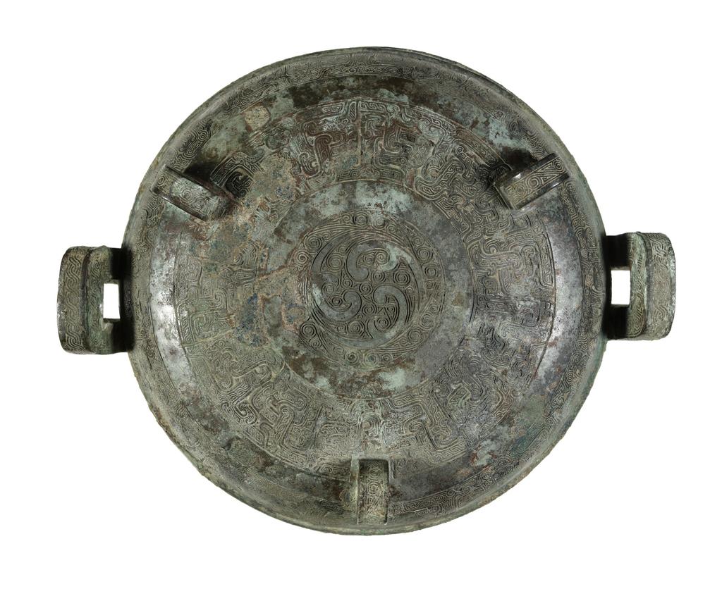 An image of Ting with cover, bronze, double loop handles at the sides with three rings, superbly chiselled with a scroll motif in the centre, and engraved with bands of intertwined archaic fret which are repeated in two zones on the body, supported on three eabriole legs with ogre masks in low relief, green patination with slight reddy-brown markings, the interior with blue and green encrusted patina. Chinese, circa 481 to 221 B.C.