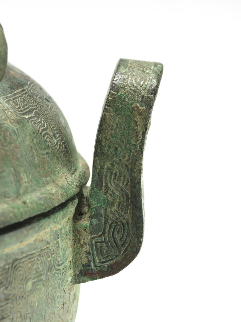 An image of Ting with cover, bronze, double loop handles at the sides with three rings, superbly chiselled with a scroll motif in the centre, and engraved with bands of intertwined archaic fret which are repeated in two zones on the body, supported on three eabriole legs with ogre masks in low relief, green patination with slight reddy-brown markings, the interior with blue and green encrusted patina. Chinese, circa 481 to 221 B.C.