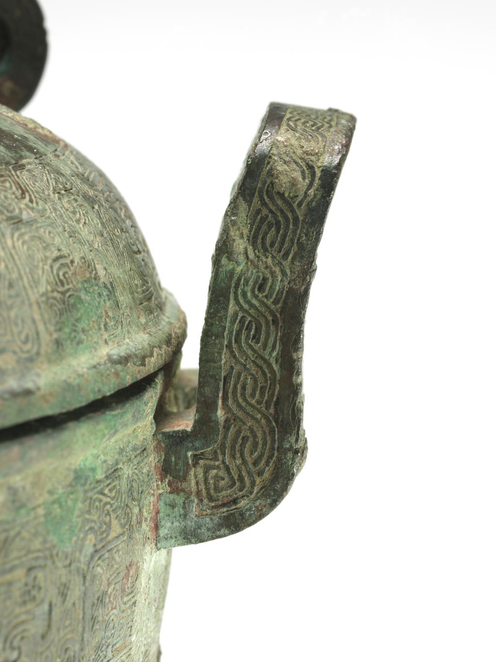 An image of Ting with cover, bronze, double loop handles at the sides with three rings, superbly chiselled with a scroll motif in the centre, and engraved with bands of intertwined archaic fret which are repeated in two zones on the body, supported on three eabriole legs with ogre masks in low relief, green patination with slight reddy-brown markings, the interior with blue and green encrusted patina. Chinese, circa 481 to 221 B.C.