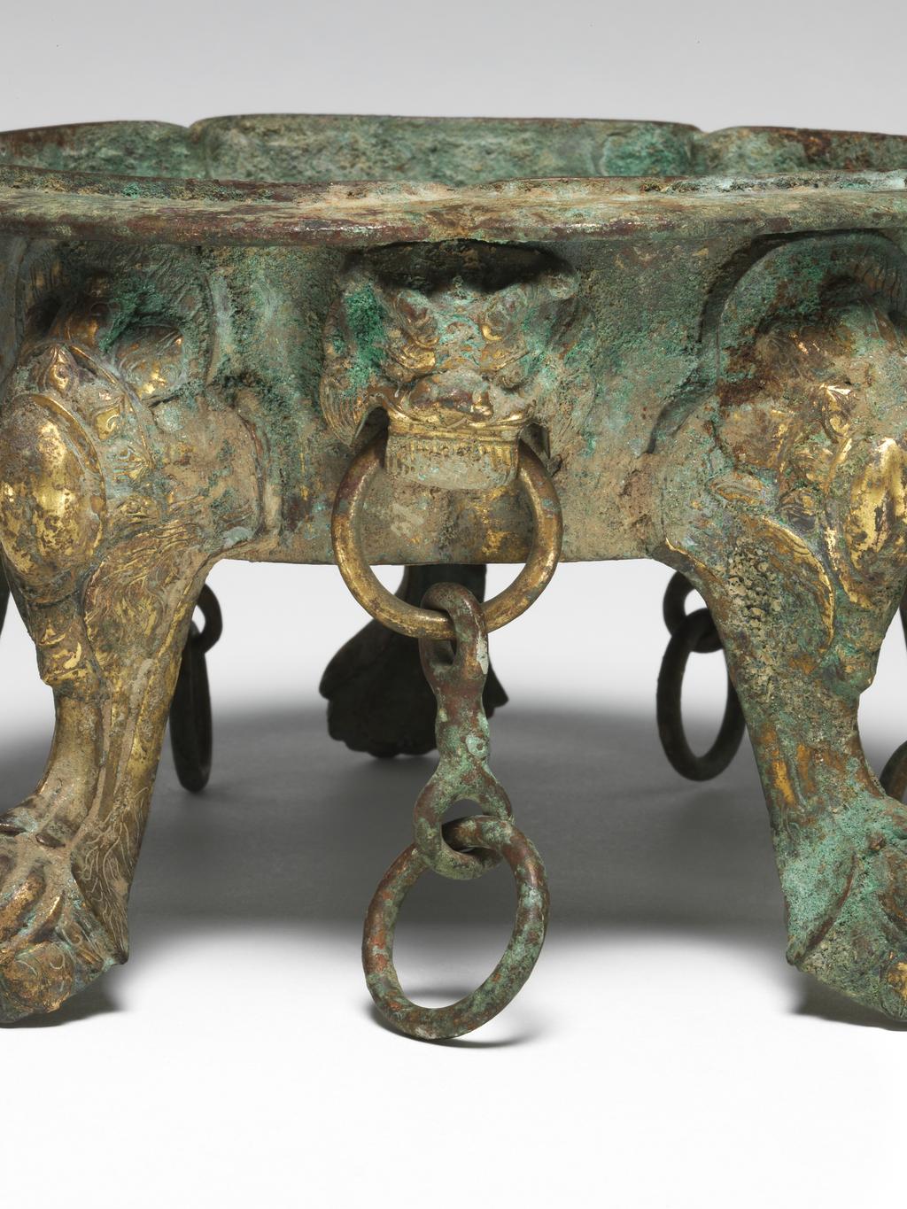 An image of Gilt-bronze censer, cast and supported on four cabriole legs, rising to an everted five-lobed rim, pierced through the sides with monster-face brackets suspending chains between each leg. Chinese, Tang dynasty. Circa 618 to 907 A.D.