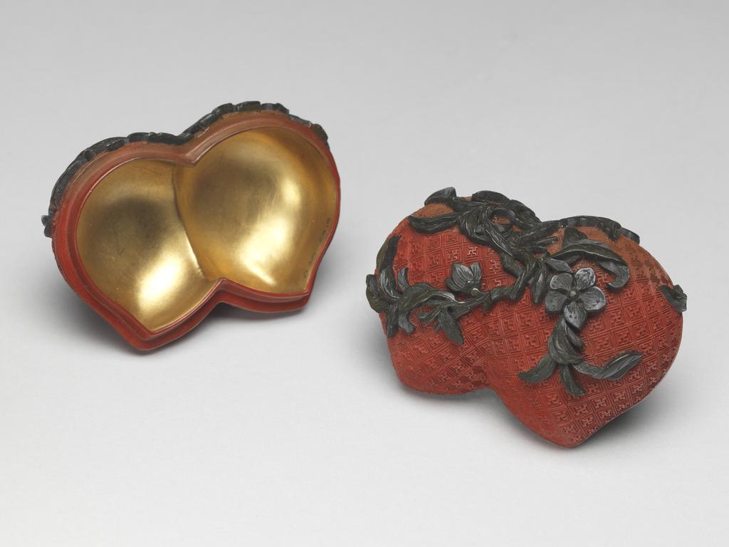 An image of A pair of small red lacquer boxes in the form of conjoined peaches, with stalks and blossoms in green lacquer, and gilding on the interior. Chinese.