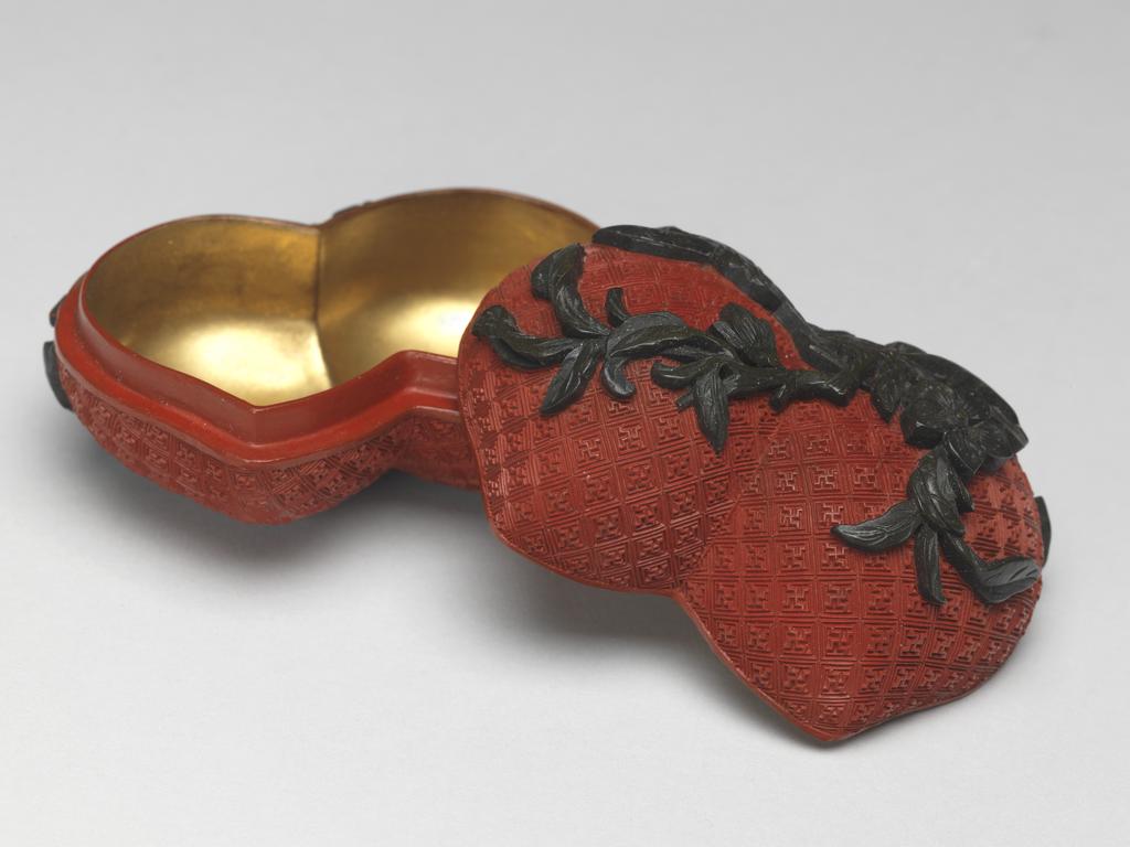 An image of A pair of small red lacquer boxes in the form of conjoined peaches, with stalks and blossoms in green lacquer, and gilding on the interior. Chinese.