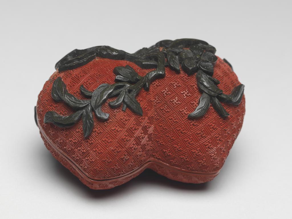 An image of A pair of small red lacquer boxes in the form of conjoined peaches, with stalks and blossoms in green lacquer, and gilding on the interior. Chinese.