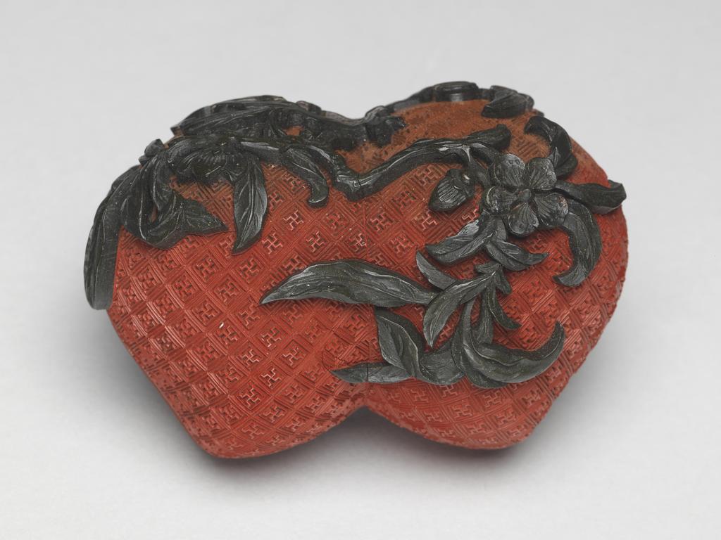 An image of A pair of small red lacquer boxes in the form of conjoined peaches, with stalks and blossoms in green lacquer, and gilding on the interior. Chinese.