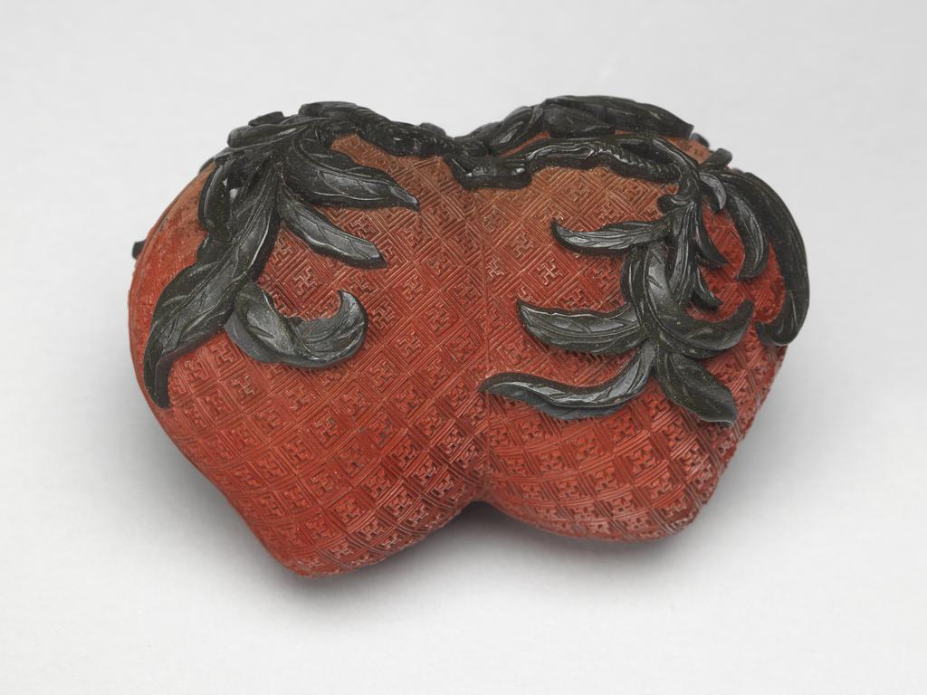 An image of A pair of small red lacquer boxes in the form of conjoined peaches, with stalks and blossoms in green lacquer, and gilding on the interior. Chinese.